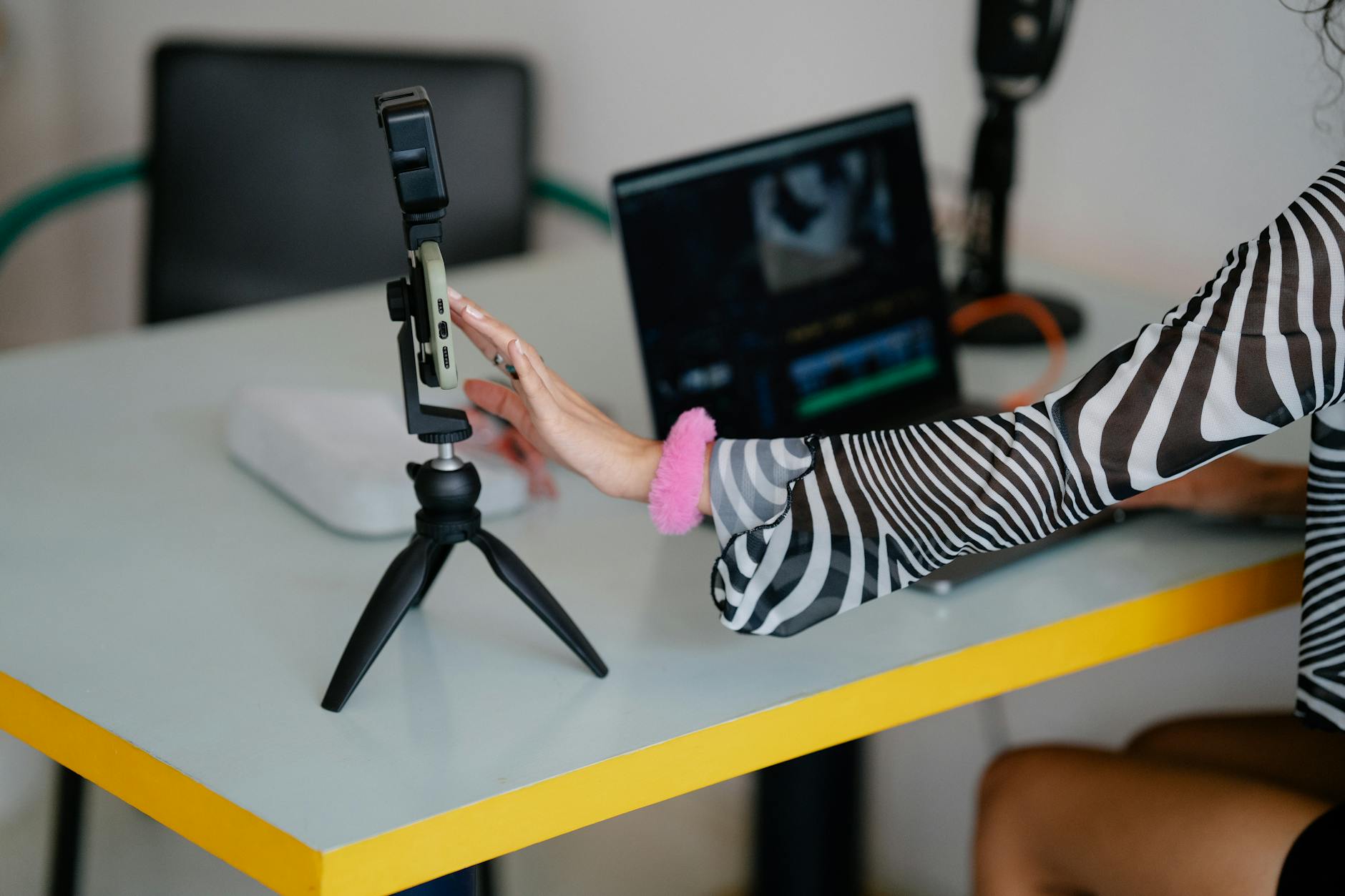 Woman editing video content on laptop with smartphone setup for content creation