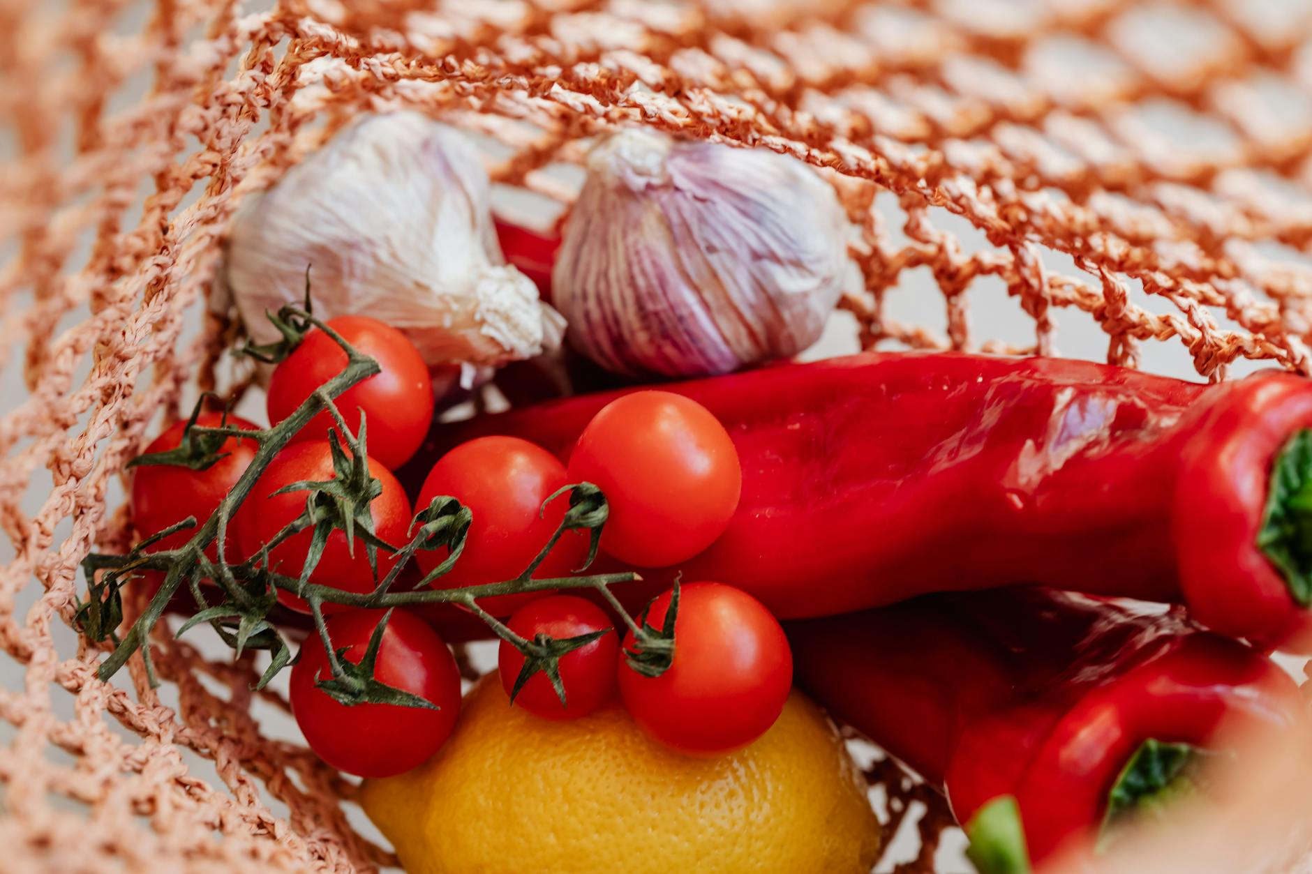 Fresh red peppers, garlic, and tomatoes in a reusable net shopping bag for a sustainable grocery run