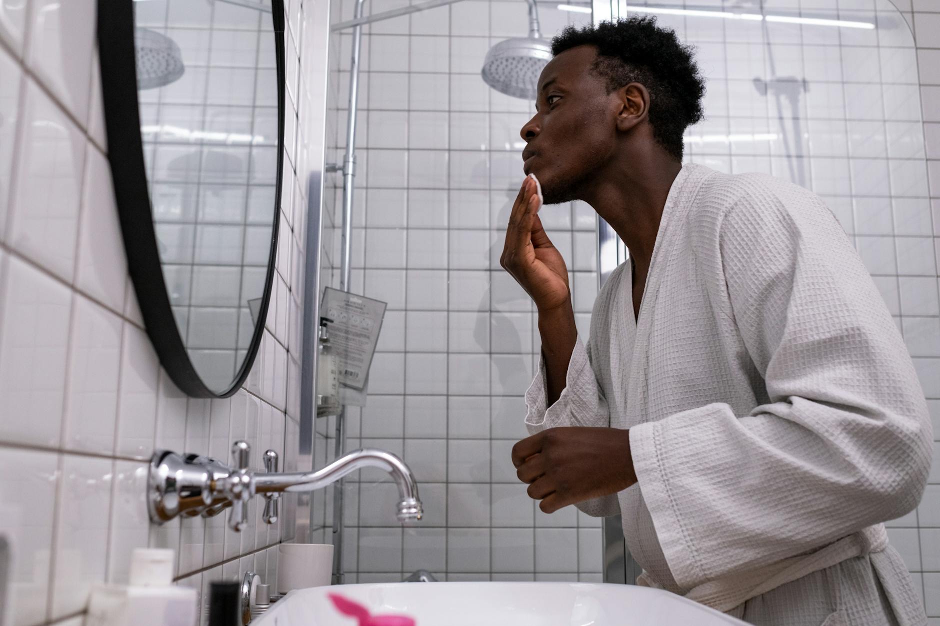 Man applying skincare products in bathroom mirror — men's grooming routine in 30s