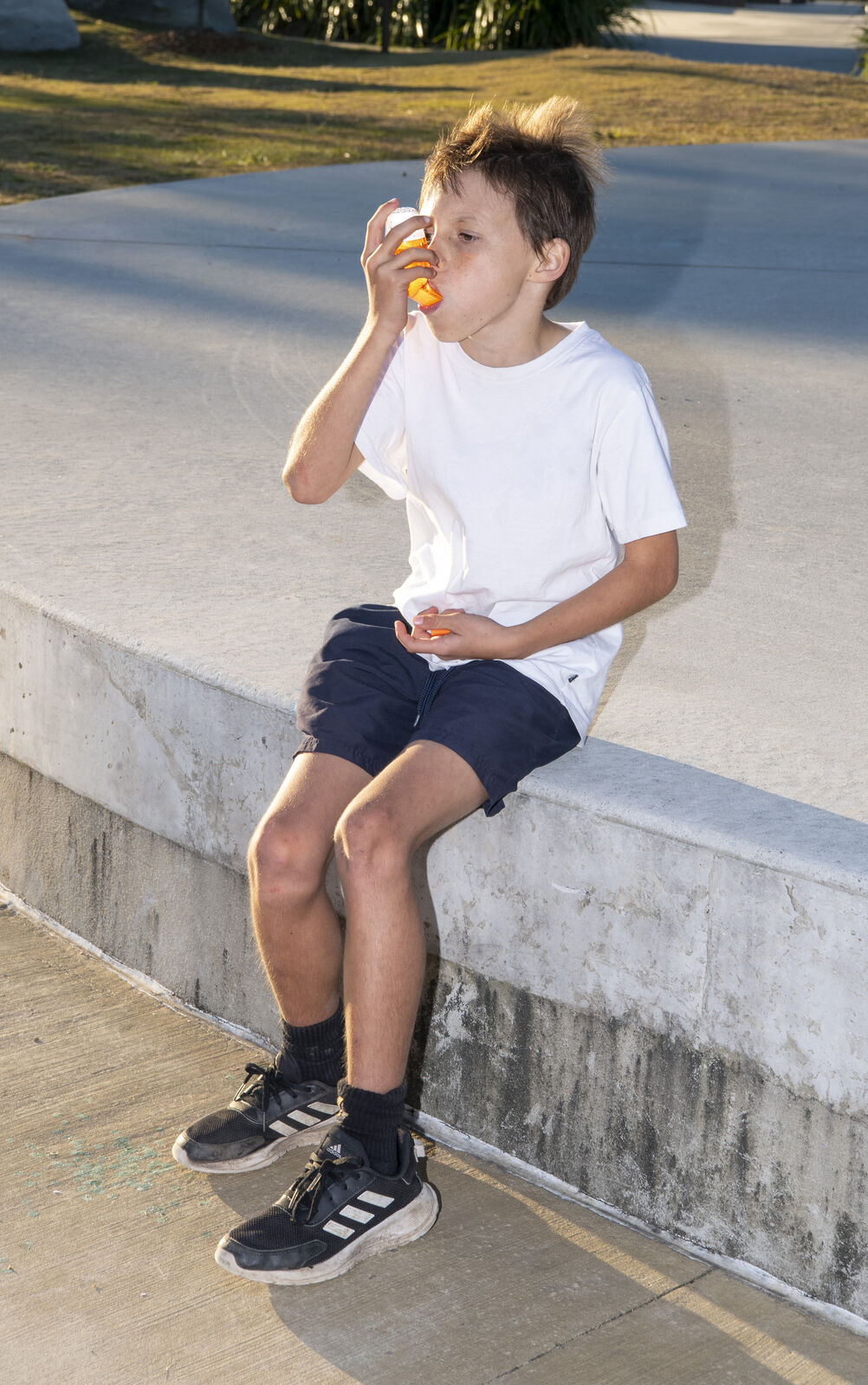 Young boy using AirPhysio for Children device outdoors on a bench