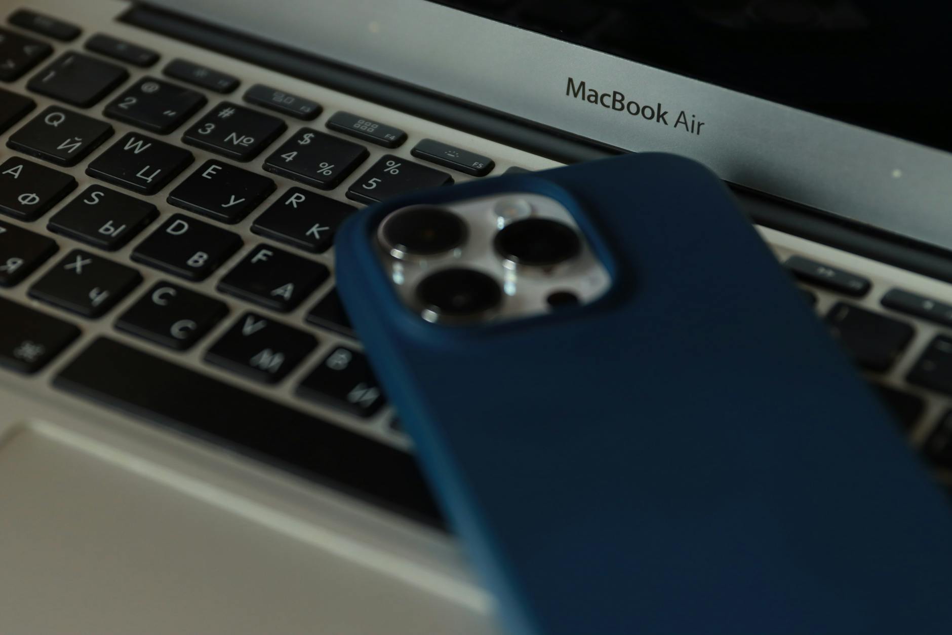 MacBook and iPhone — Apple Find My Network Relay Devices MacBook and iPhone in an office setting — Apple devices that passively relay Find My location data
