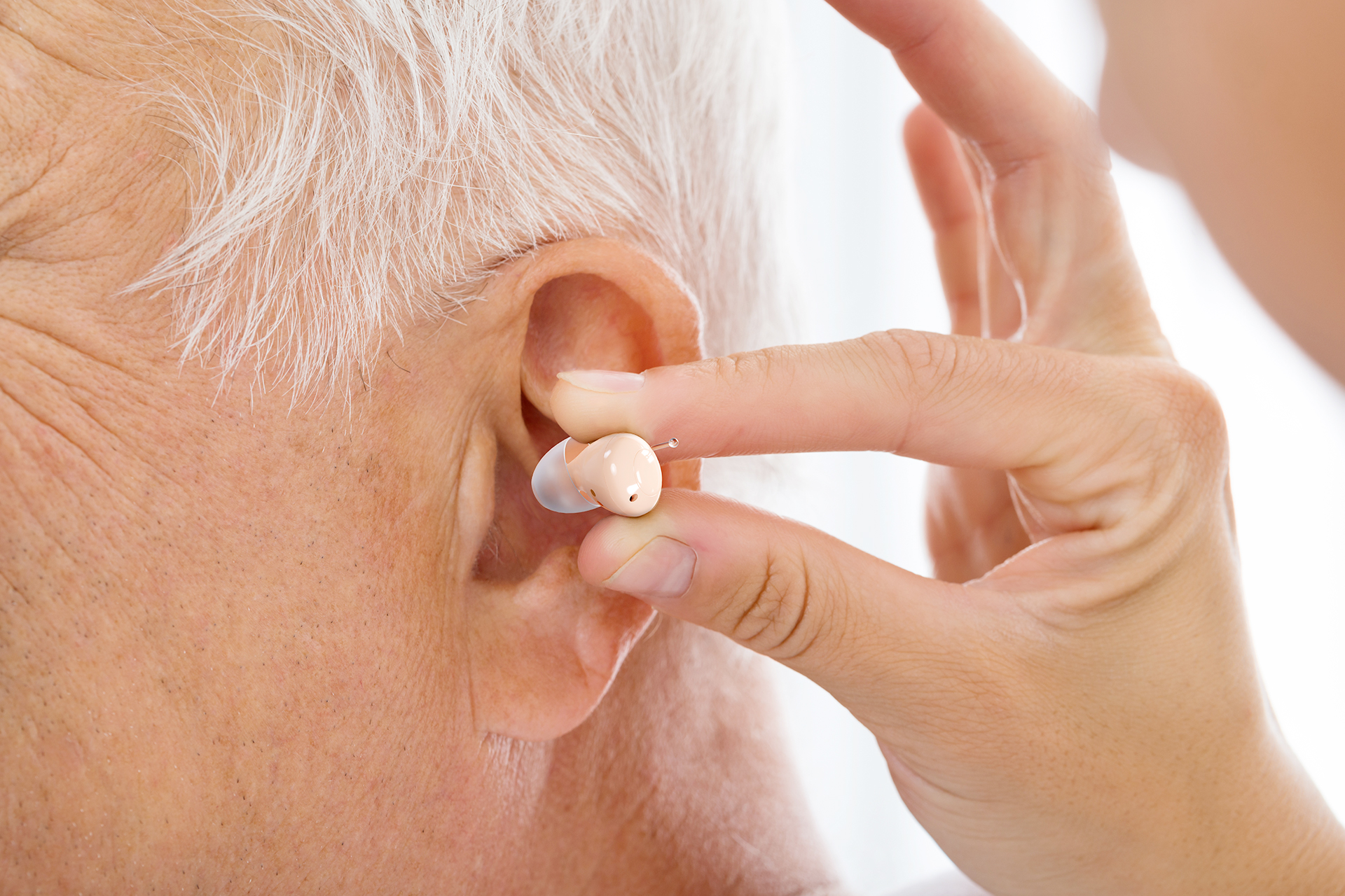 Extreme close-up of Audien Atom One hearing aid held between fingers showing tiny compact size