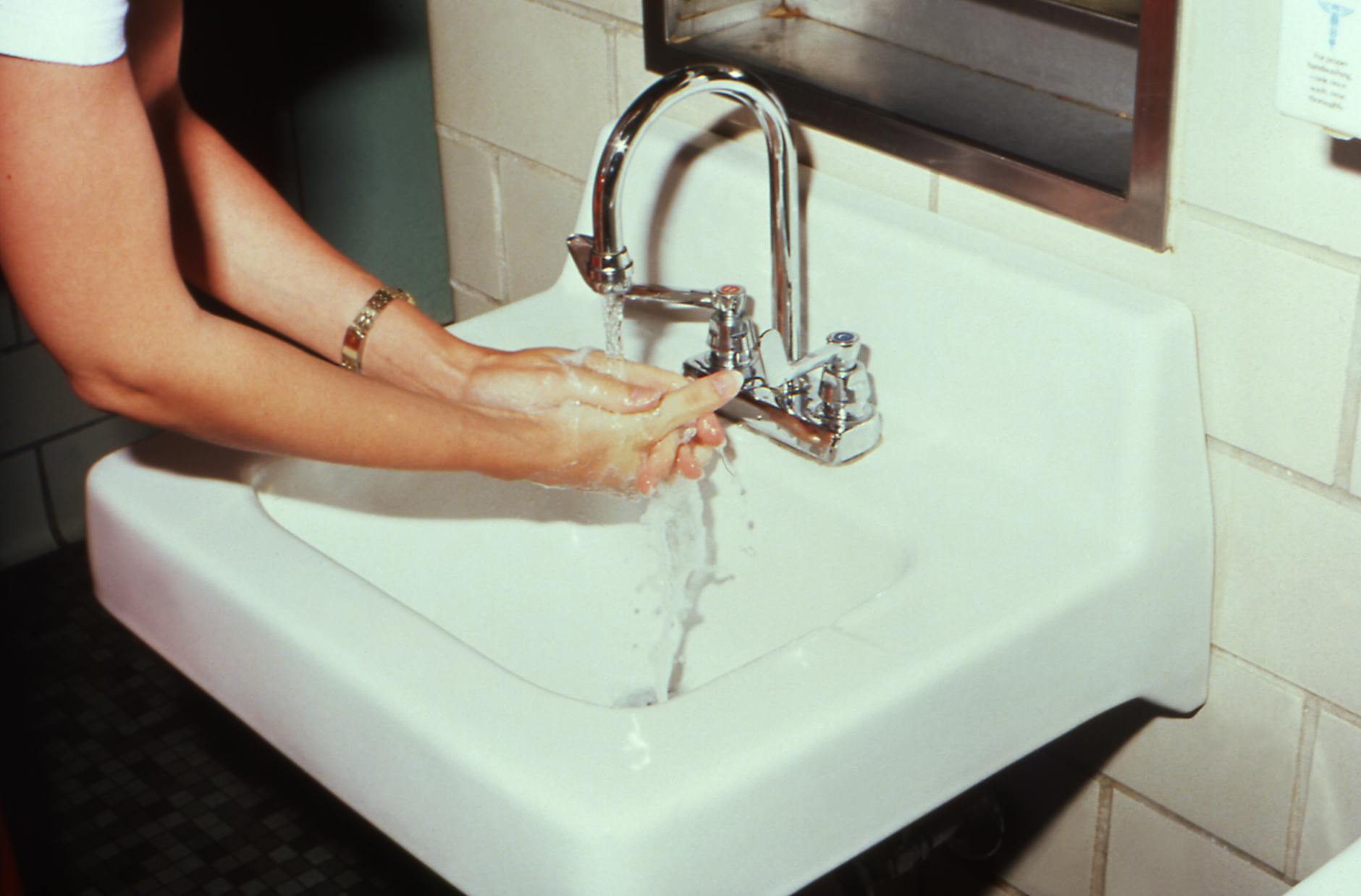 Woman washing hands at bathroom sink to prevent cross-contamination and spread of bacteria