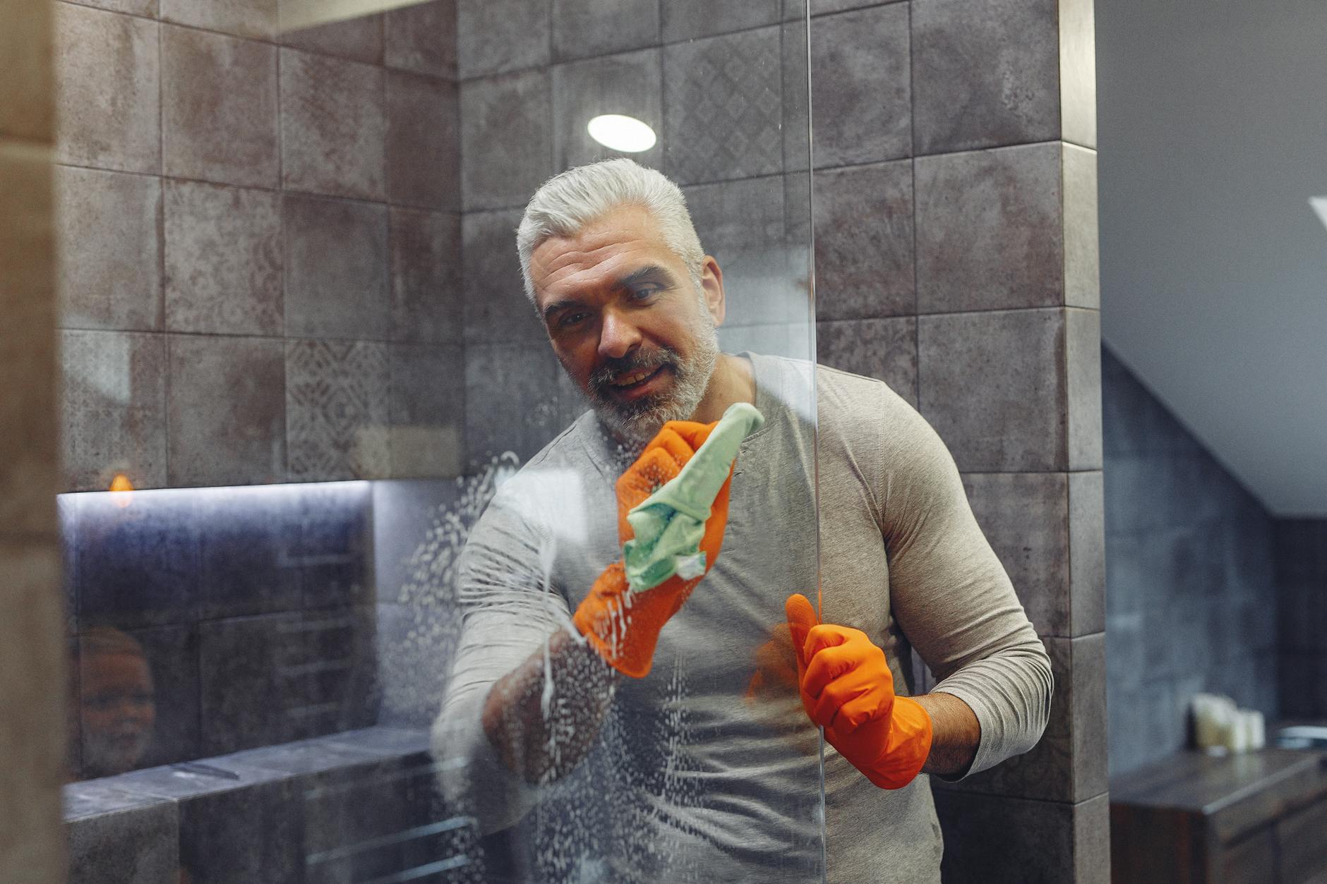 Man wearing rubber gloves cleaning a shower glass panel