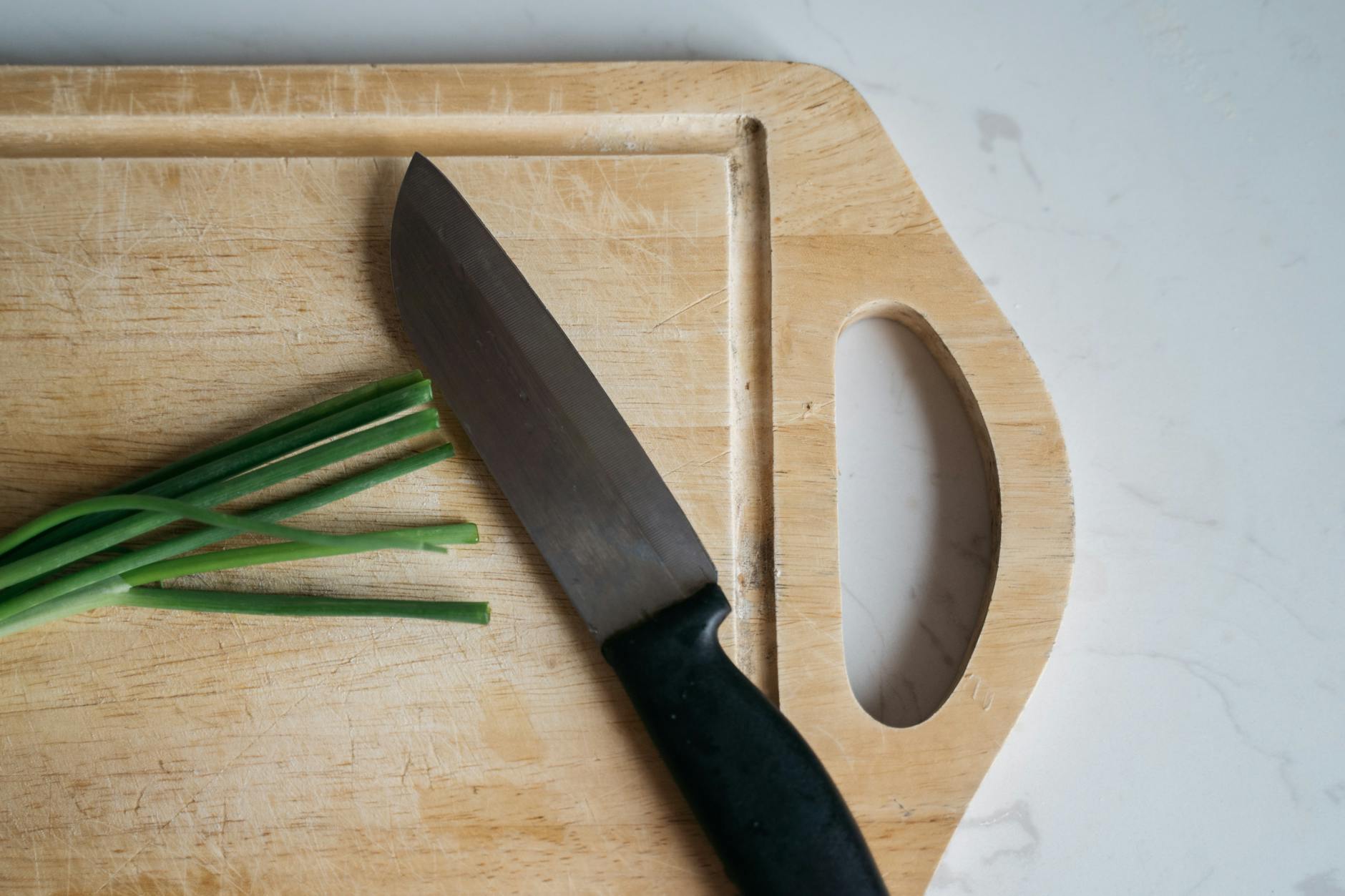Knife resting on a wooden cutting board next to fresh green onions