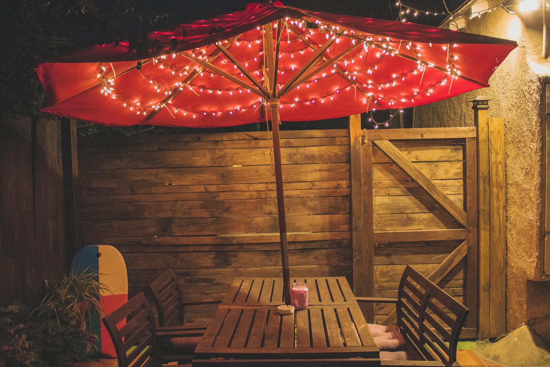Outdoor Evening Dining Setup - Outdoor Party Gift Guide 2026 Outdoor dining area with red parasol and string lights for evening entertaining