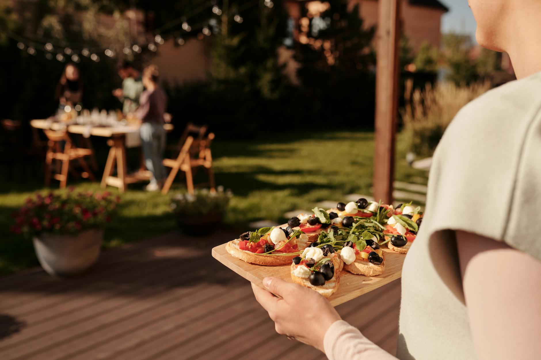 Outdoor Garden Party Hosting - Backyard Gift Ideas 2026 Woman serving appetizers on a tray at an outdoor garden party with friends