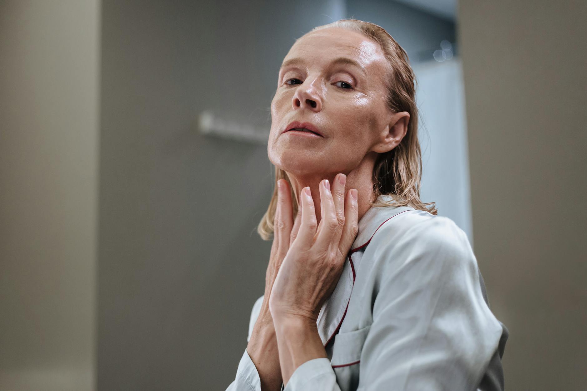 Mature woman applying skincare product in a bathroom — managing facial hair changes with age
