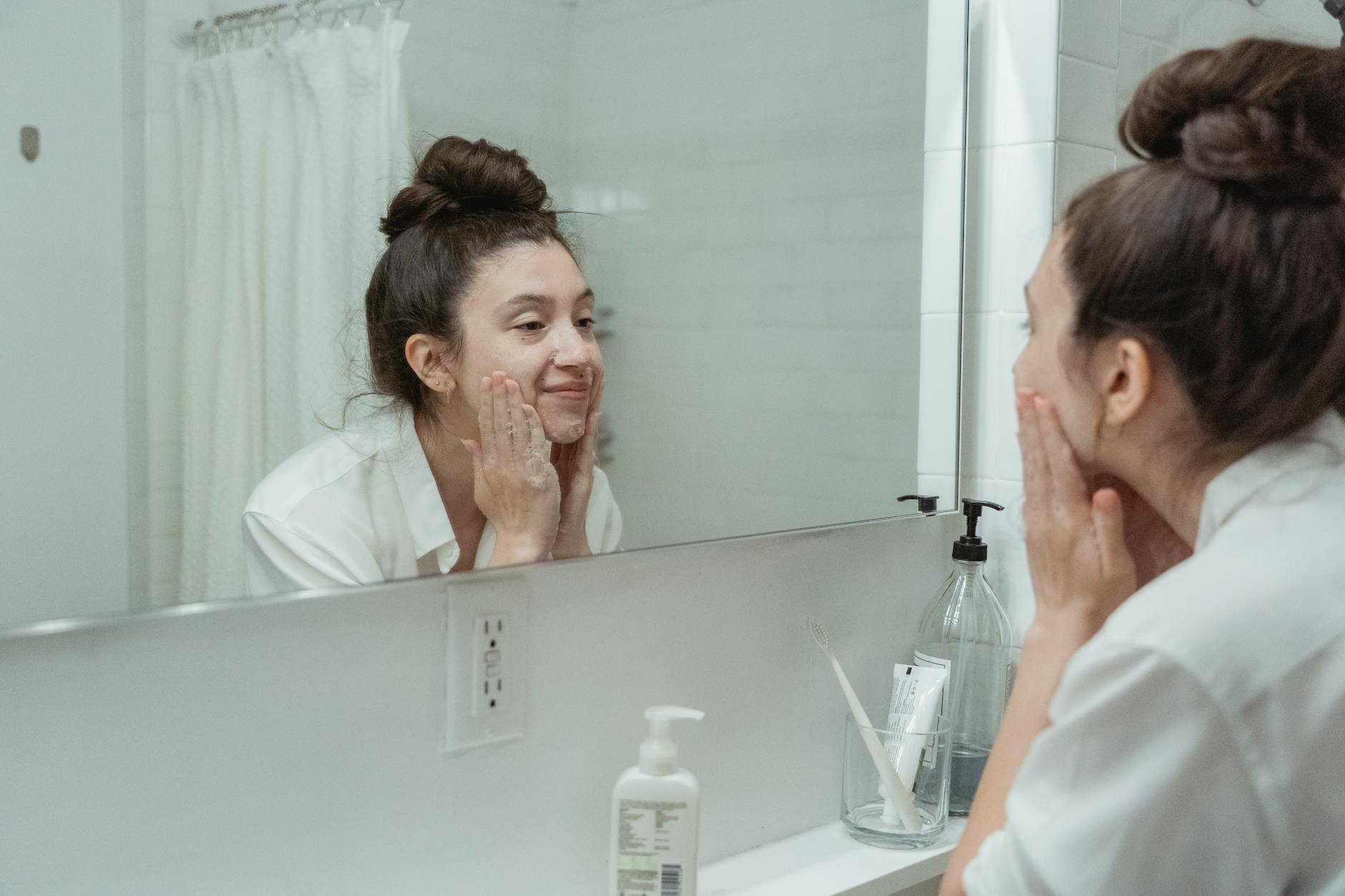 Woman examining her face in a bathroom mirror during a skincare routine