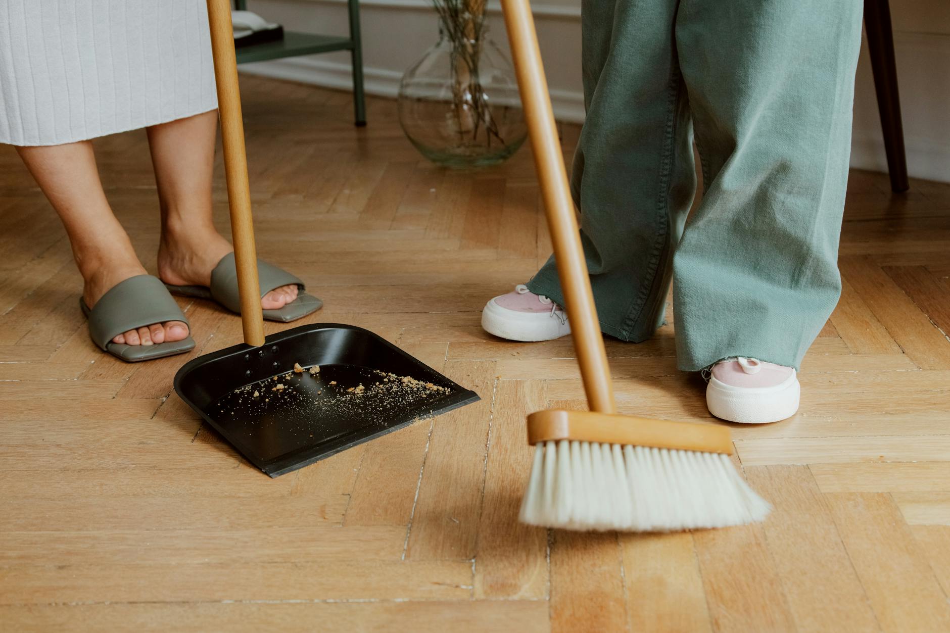Person sweeping wooden floor with broom and dustpan before mopping — proper floor cleaning order