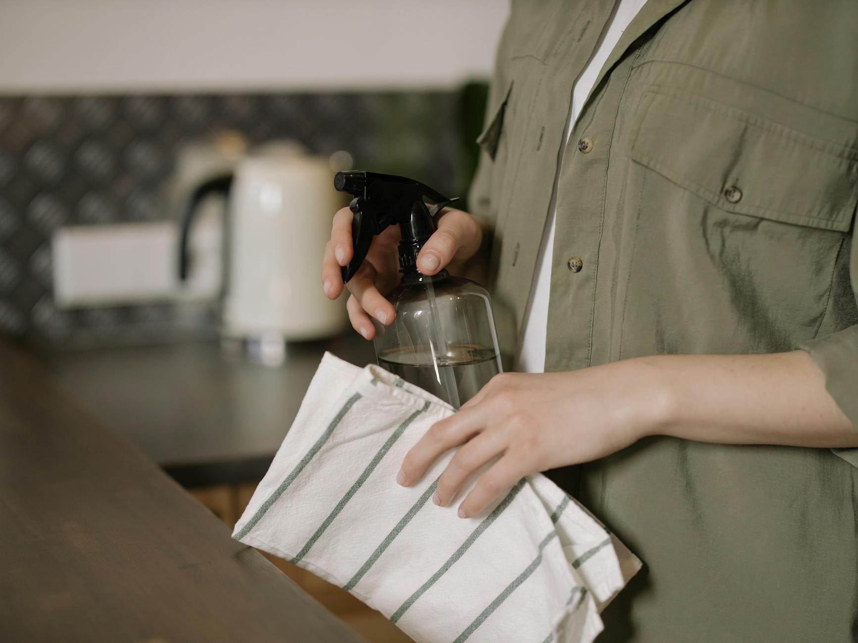 A person spraying and wiping a kitchen counter with a cloth, demonstrating proper technique