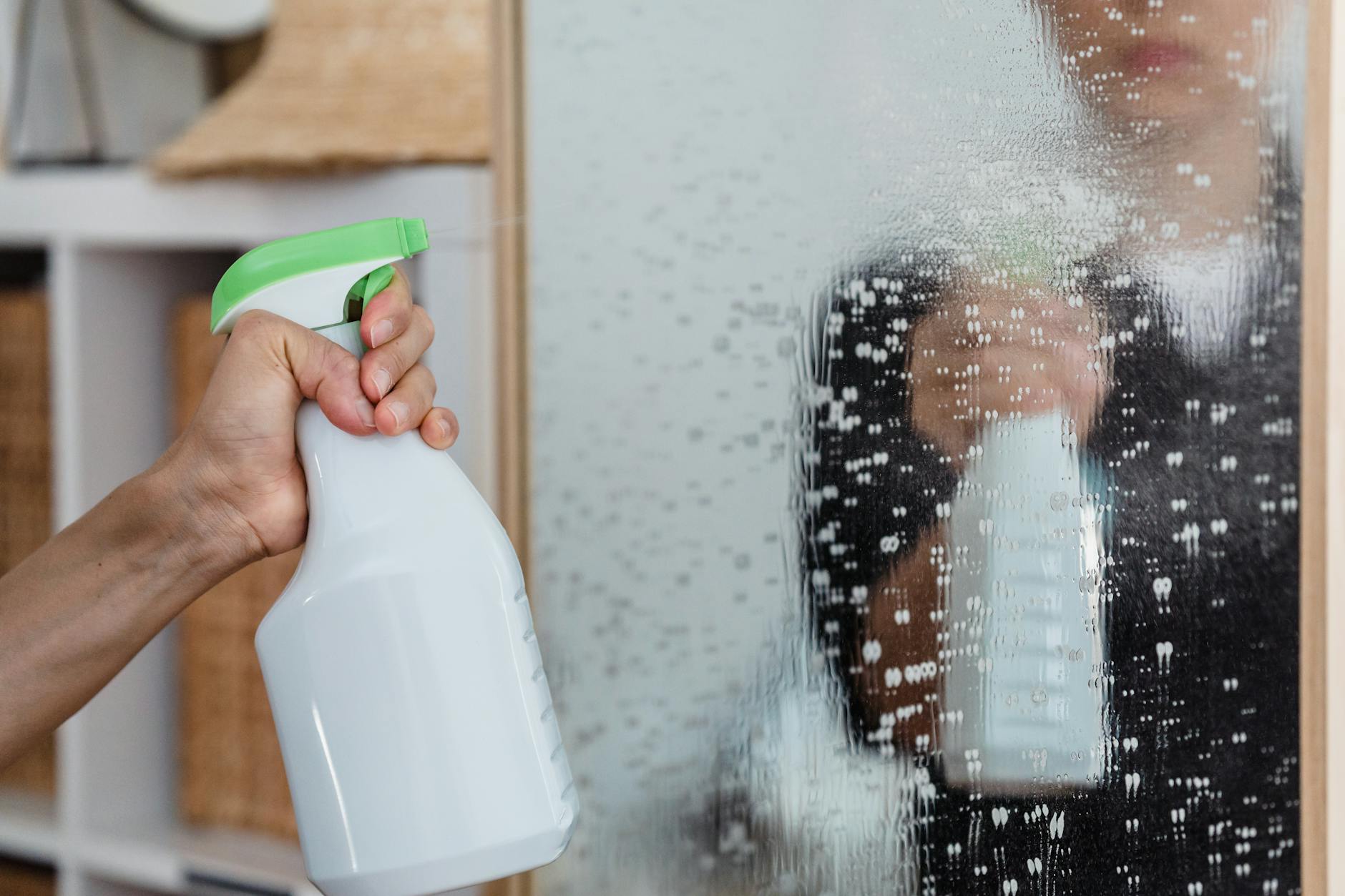 Hand using spray bottle to clean a mirror — using too much product is a common cleaning mistake