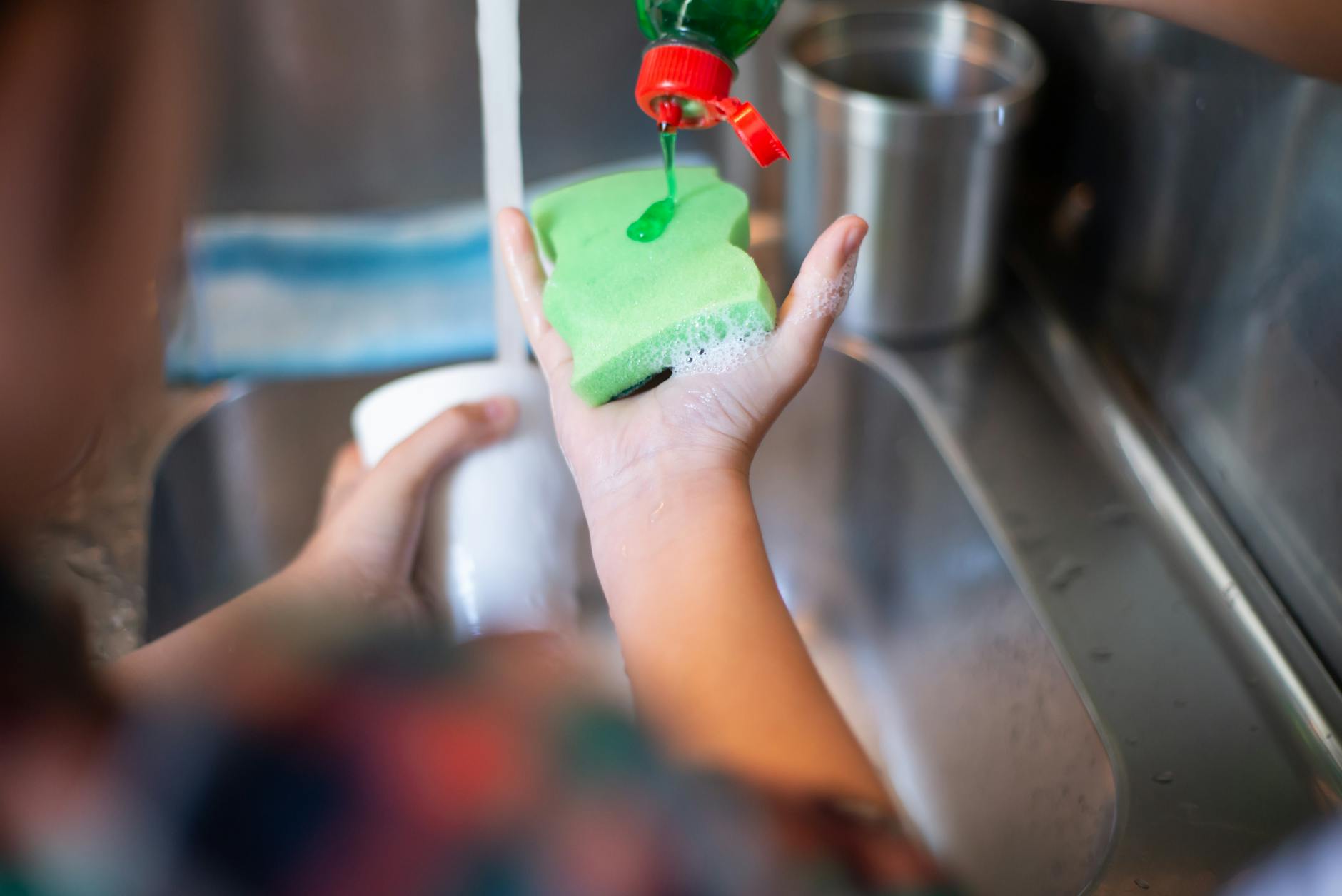 Applying dish soap to a sponge before scrubbing a cutting board in the kitchen sink