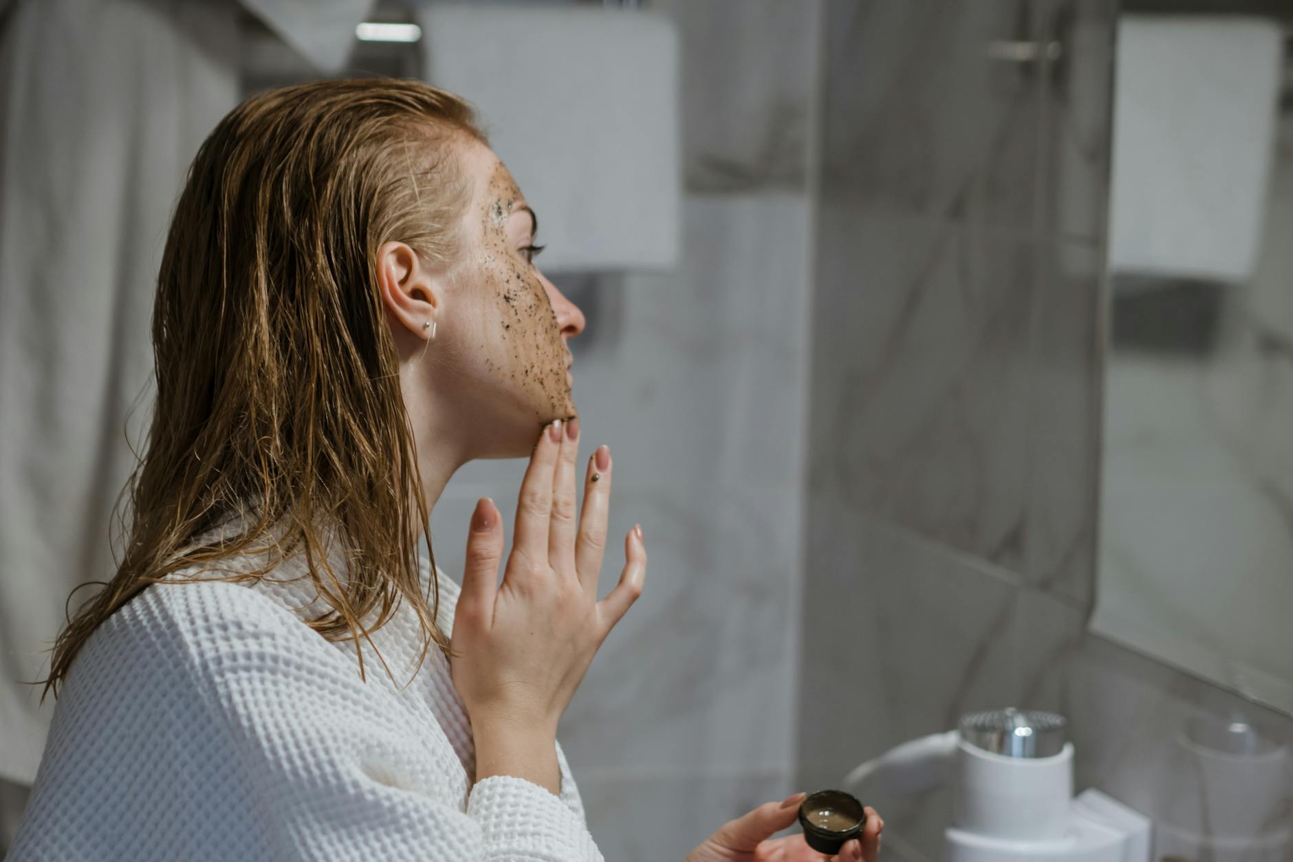Woman applying facial scrub exfoliation treatment at home in bathroom
