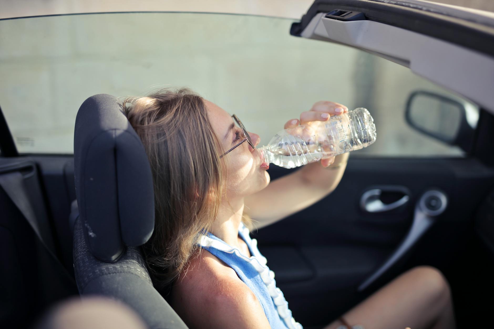 Woman drinking from a water bottle while seated in a car — illustrating the distraction risk of unsecured drinks