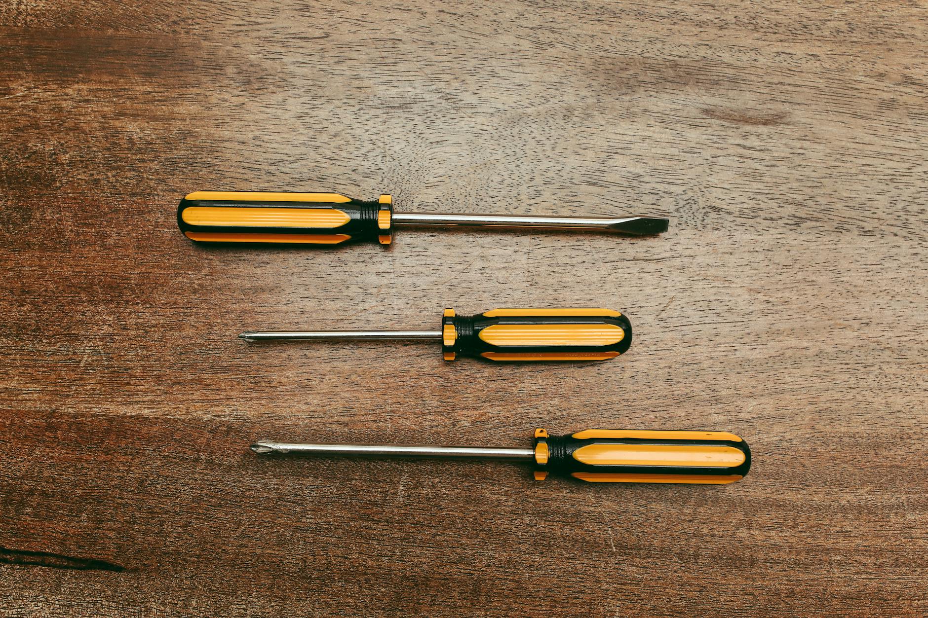 Three screwdrivers laid flat on a wooden table for simple home repairs