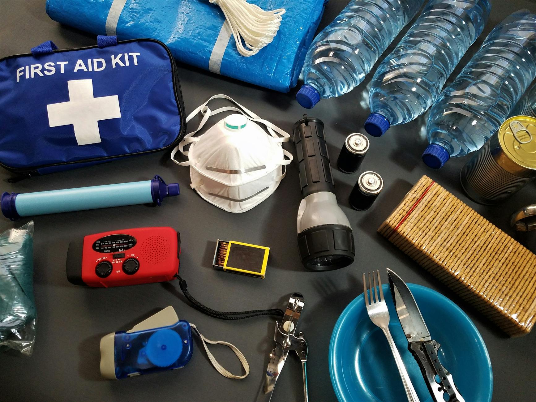 Emergency survival kit with water bottles, food supplies, and essential items laid out flat
