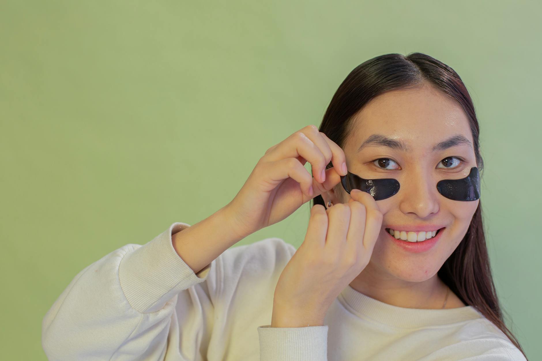 Under Eye Skincare Routine Techniques for Aging Skin Woman smiling while applying under-eye patches as part of her anti-aging eye care routine