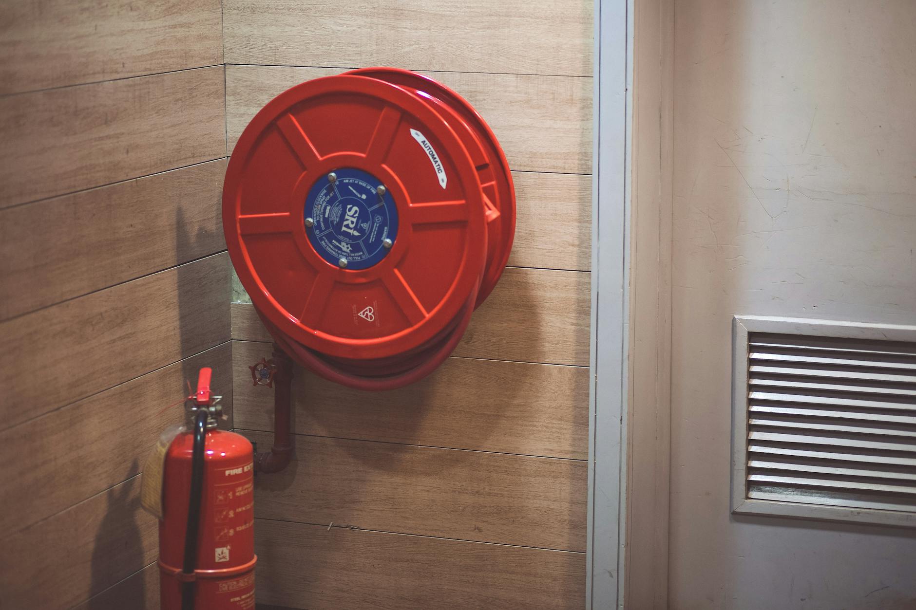 Red fire hose reel and extinguisher mounted in a building corner demonstrating proper positioning