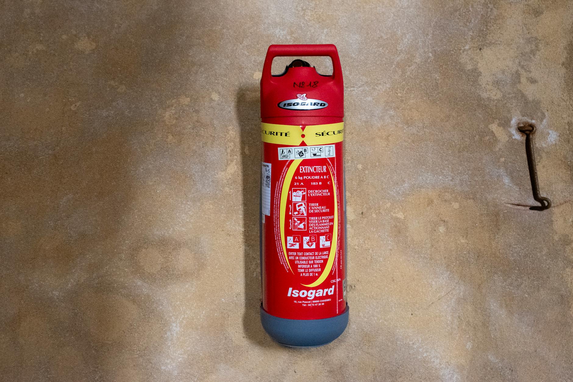 Red Isogard fire extinguisher properly mounted on a textured wall ready for use