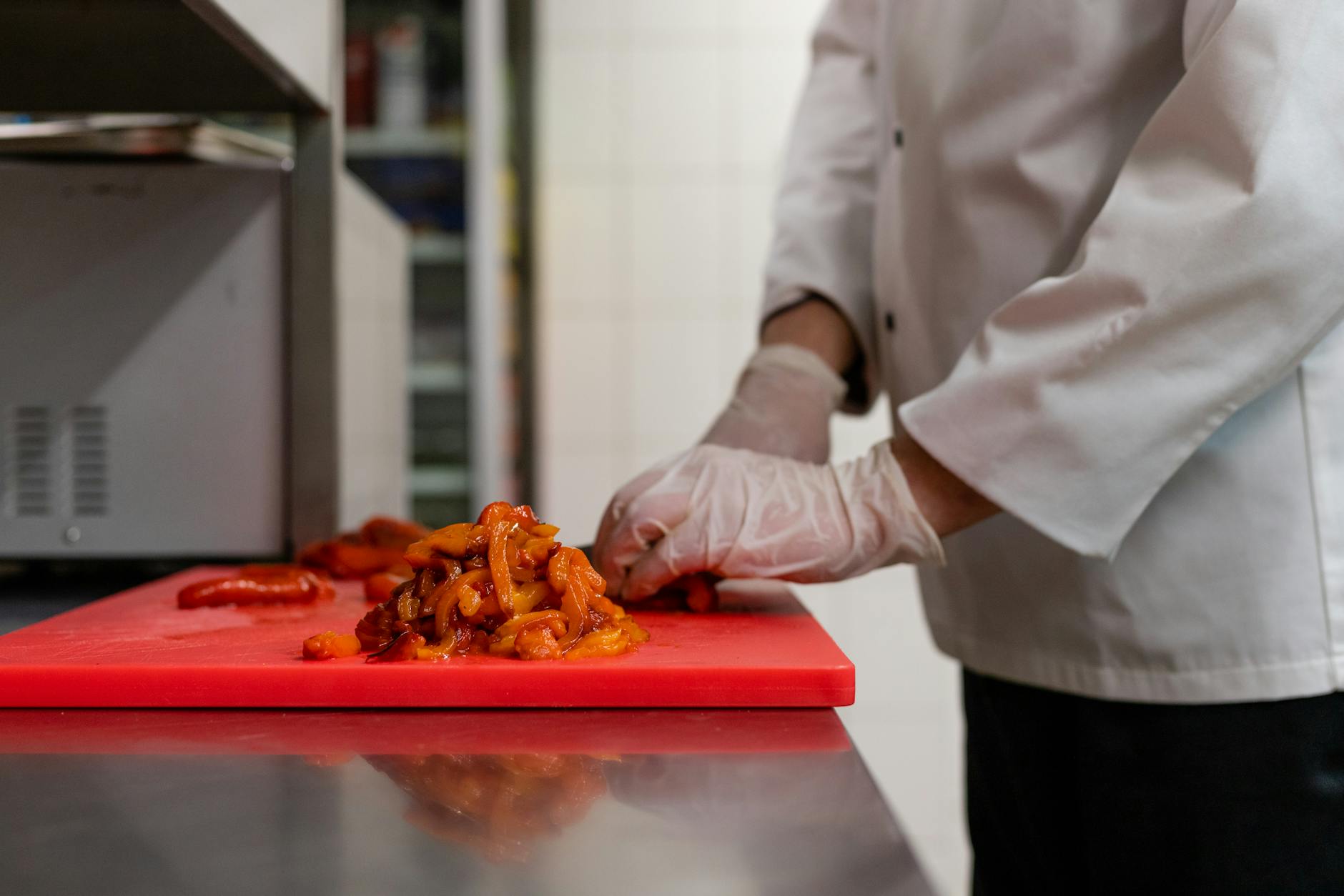 Chef chopping vegetables on a red color-coded cutting board in a kitchen — color-coded boards prevent cutting board cross contamination