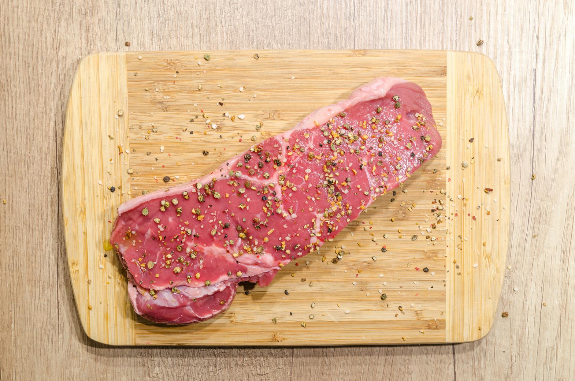 Raw beef steak on a wooden cutting board illustrating cutting board cross contamination risk