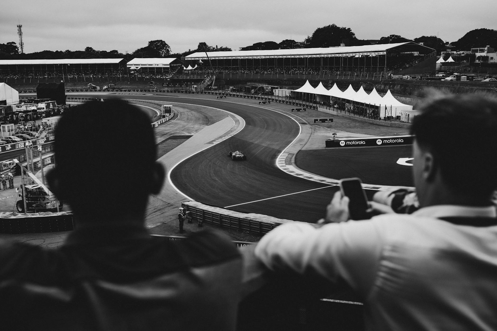 Motorsport spectators watching racing from the stands in black and white
