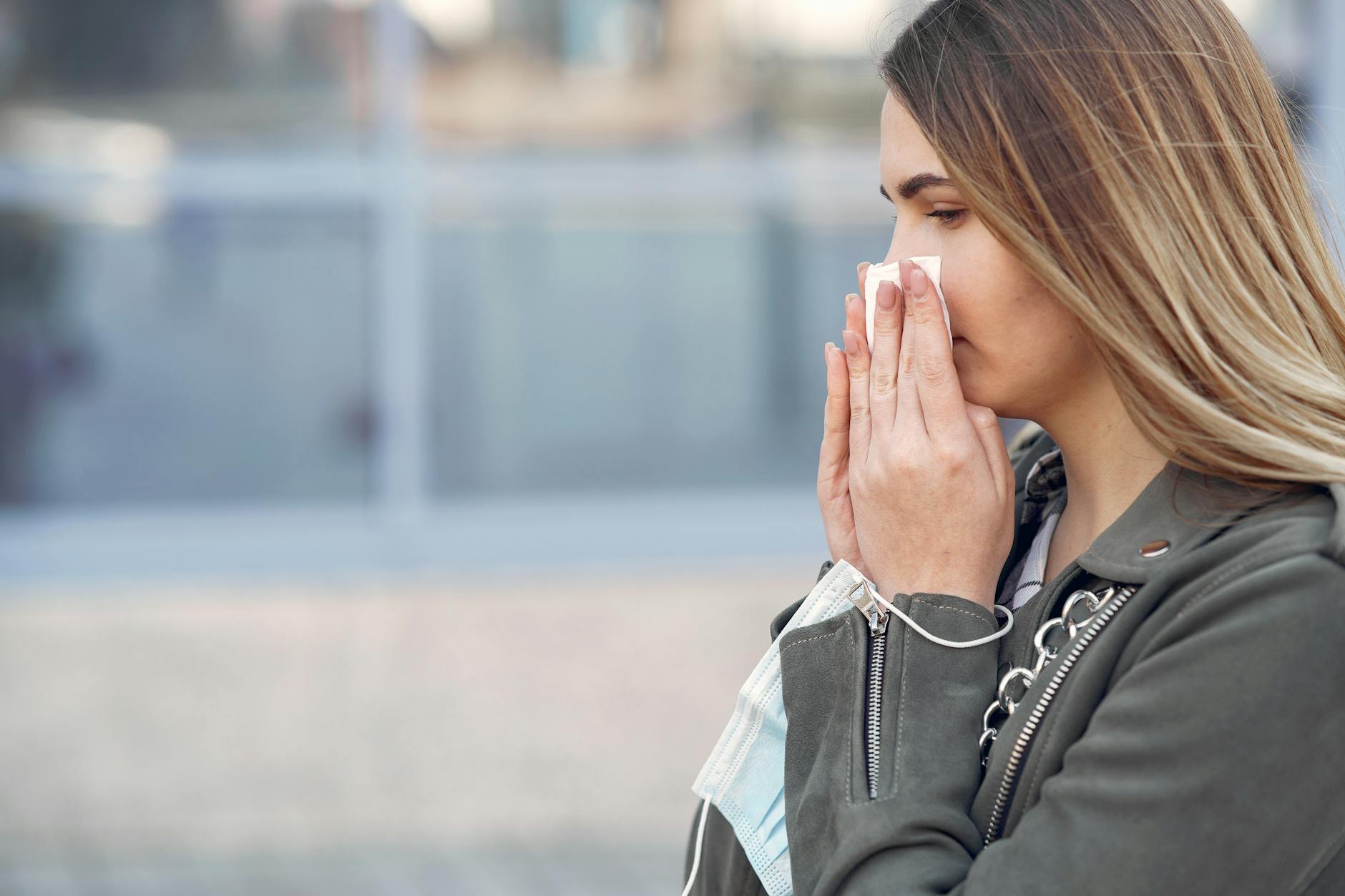 Fragrance Sensitivity Symptoms - Sneezing and Nasal Irritation Woman sneezing and holding a tissue outdoors, a common fragrance sensitivity symptom