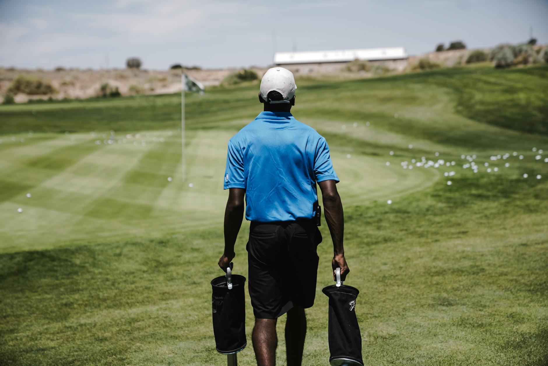 Golfer walking on a sun-drenched course fairway surrounded by lush green trees