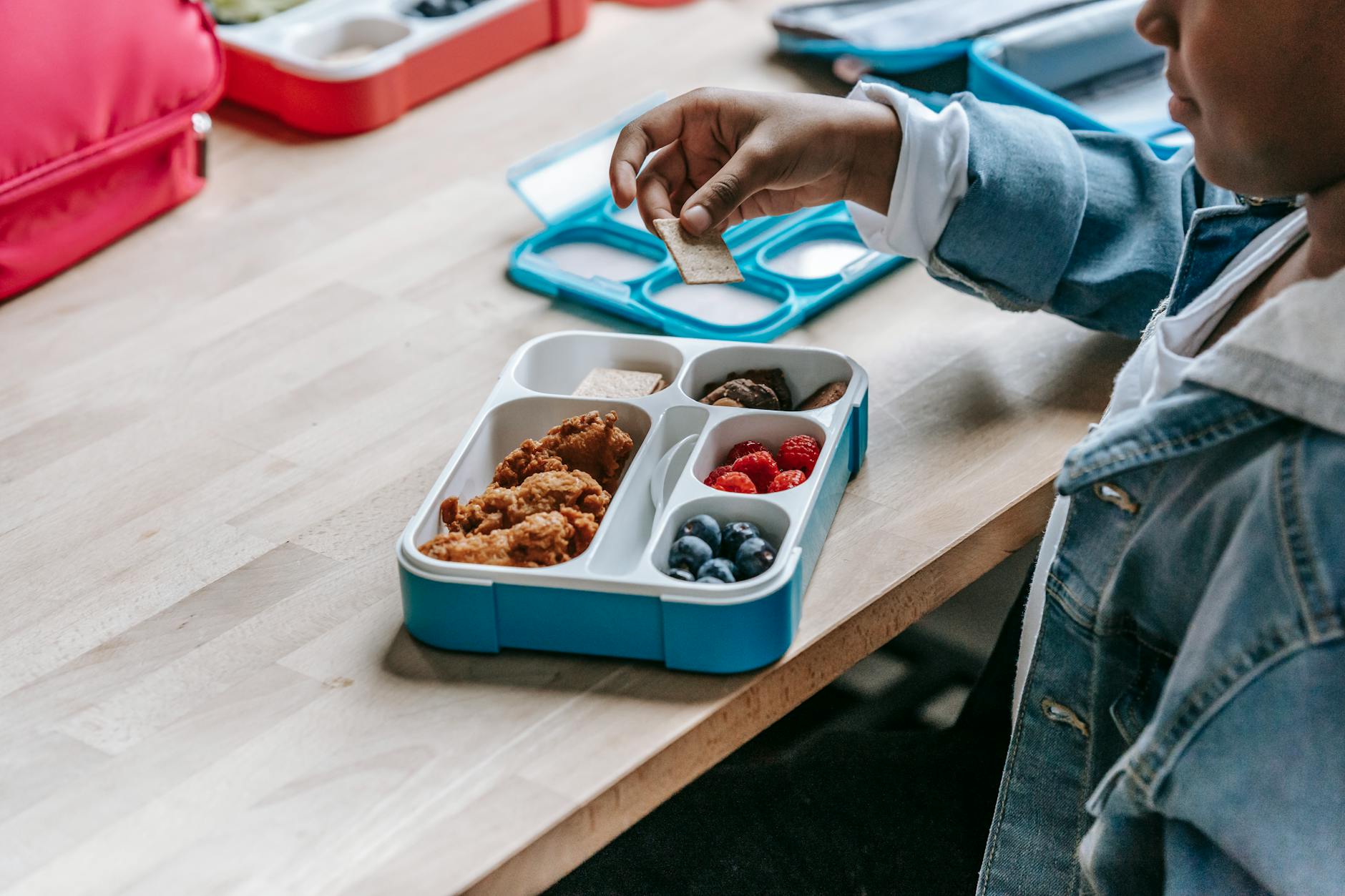 School-age child at a table with a healthy packed lunch container and drink