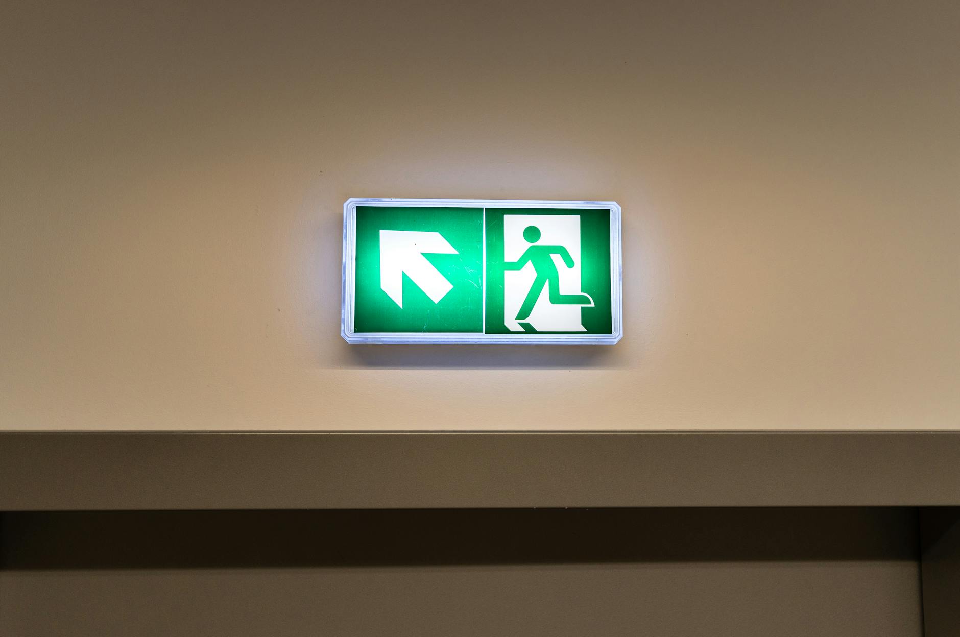 Bright green emergency exit sign with directional arrow in an indoor hallway — a key element of any fire escape route
