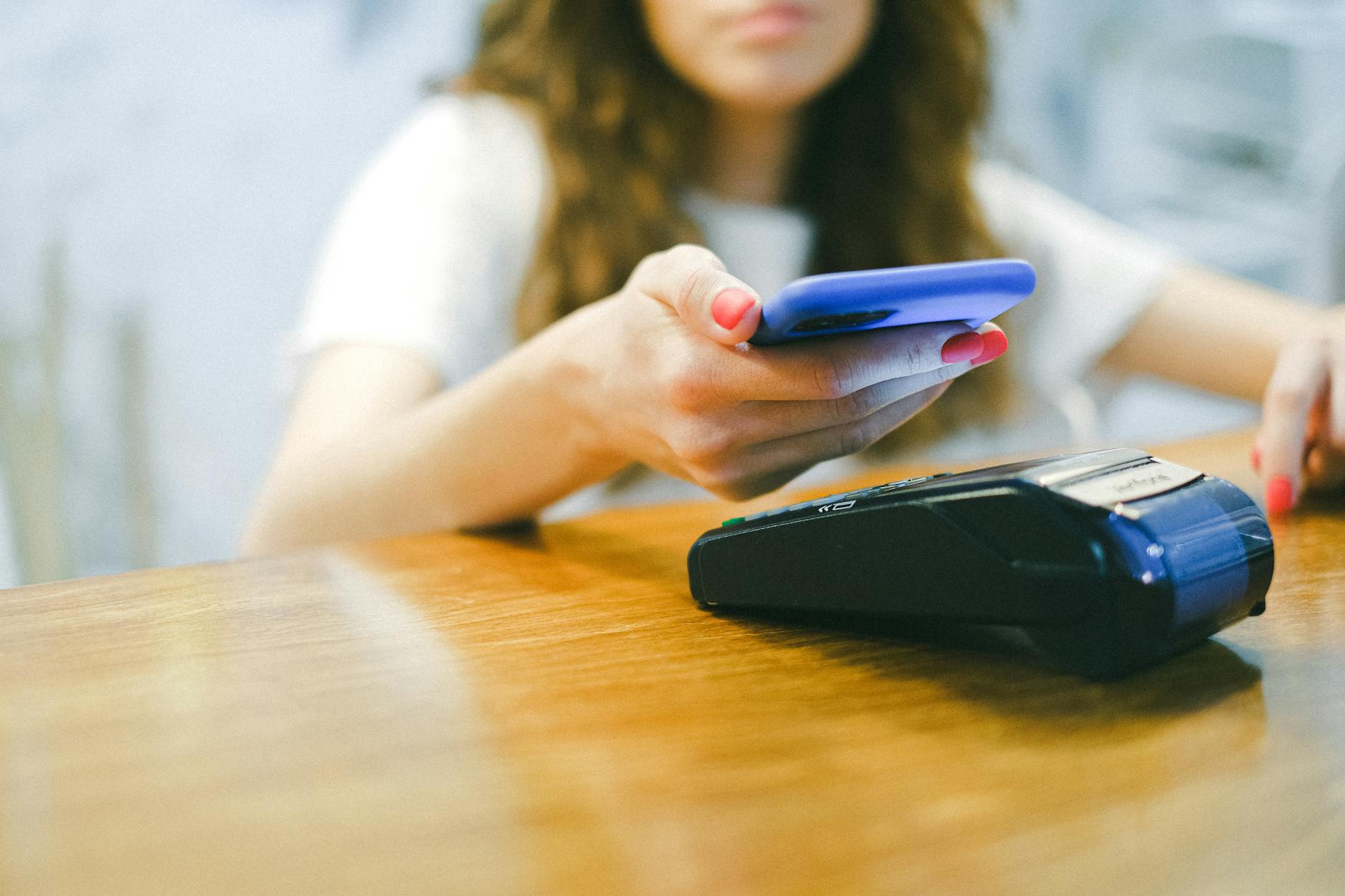 Woman using smartphone NFC tap to pay at payment terminal