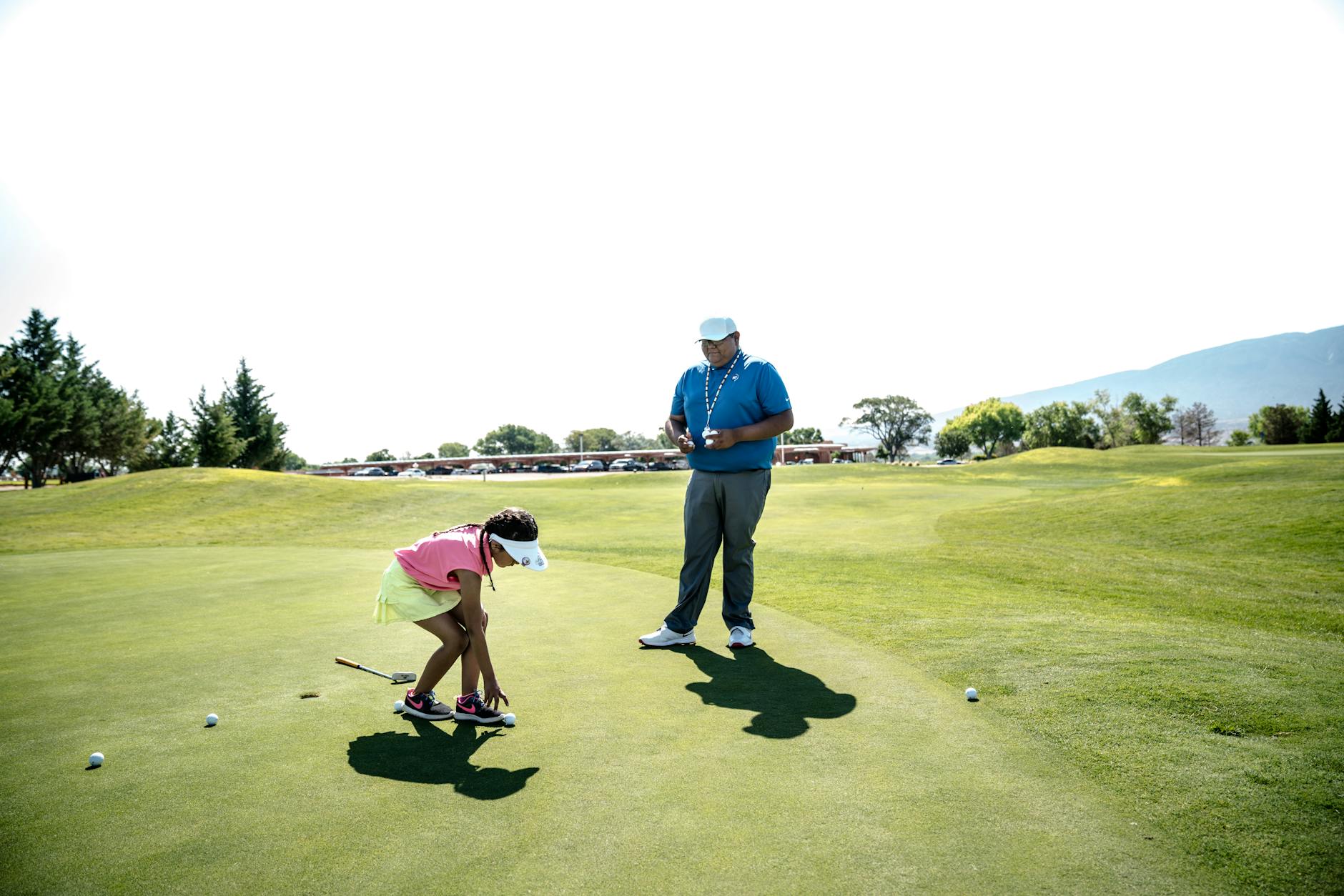 Golf instructor teaching a young beginner golfer on a sunny course