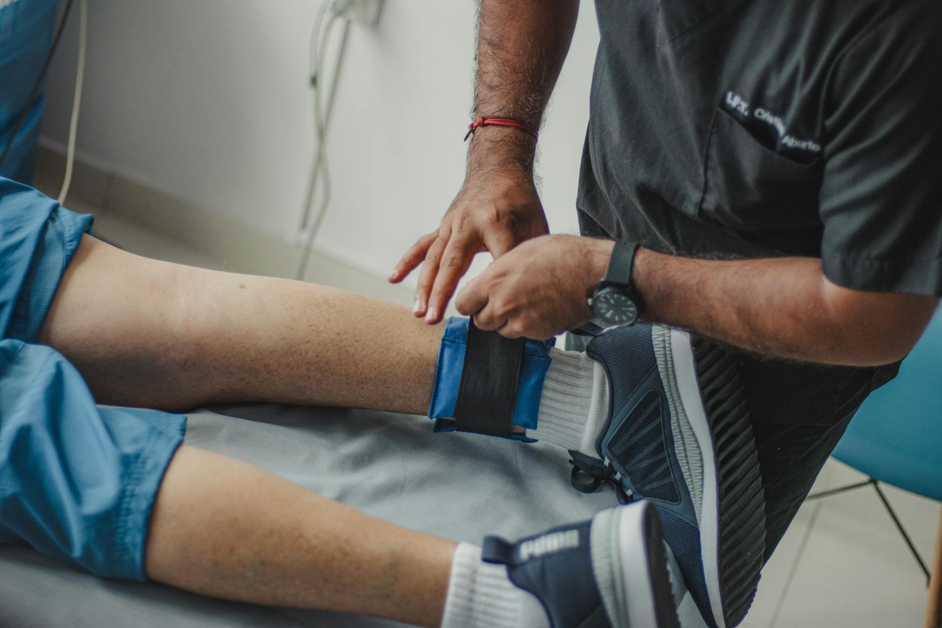 Electrical Muscle Stimulation Clinical Application Physiotherapist adjusting electrode placement on a patient's leg in a clinical setting