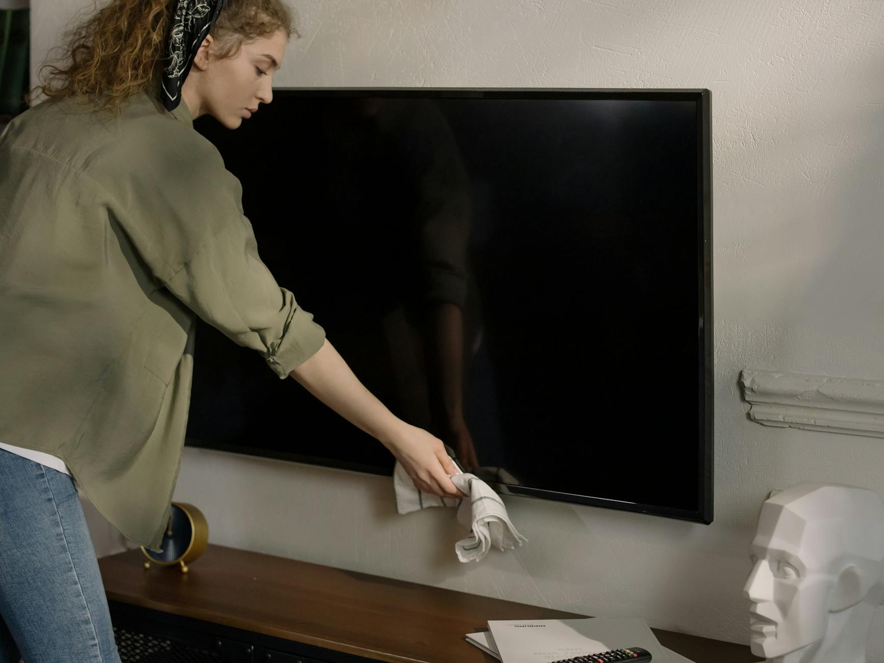 Cleaning a TV Screen Safely at Home Woman cleaning a TV screen at home with a cloth