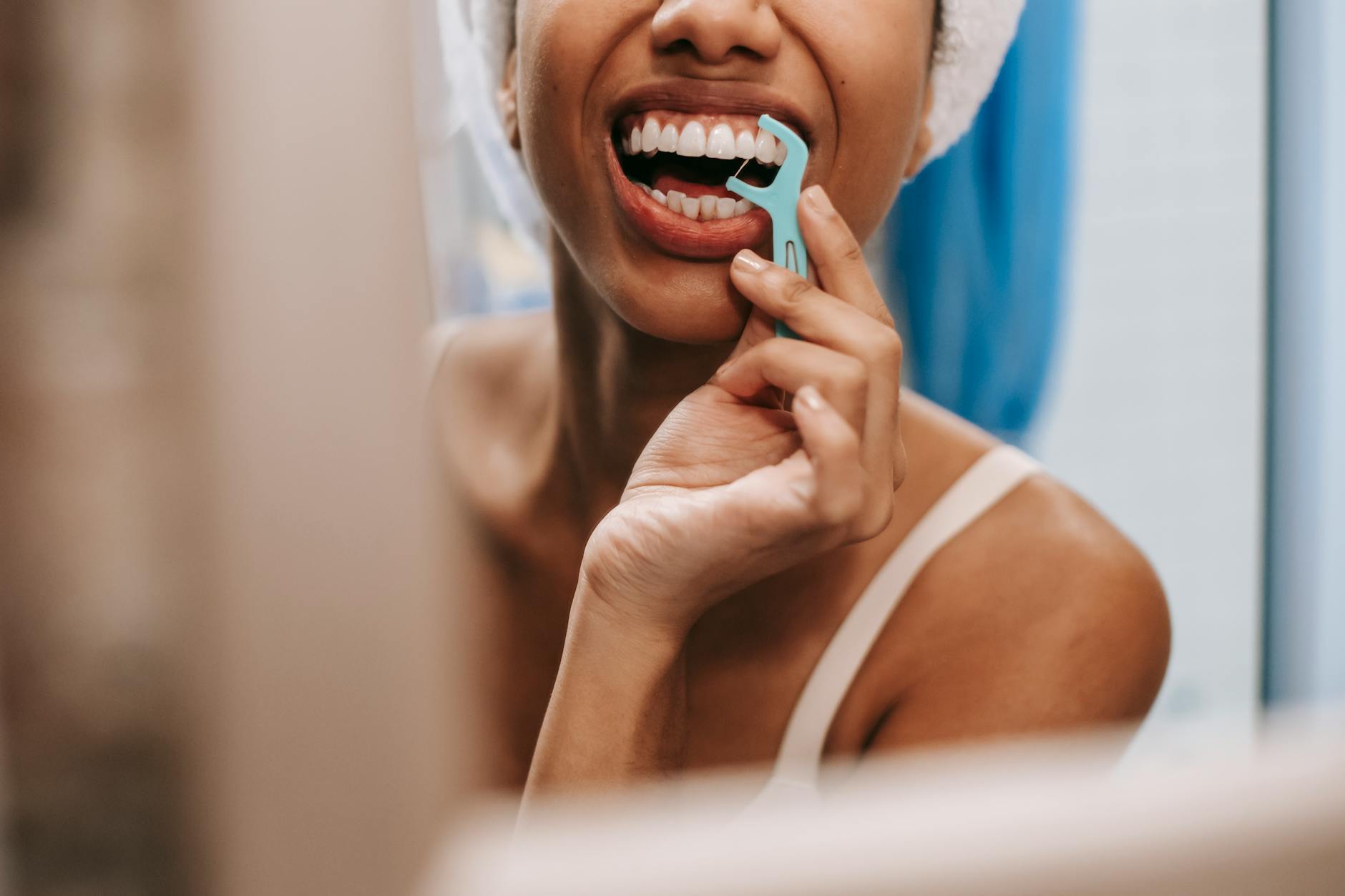 Woman flossing teeth in front of bathroom mirror as part of oral hygiene routine