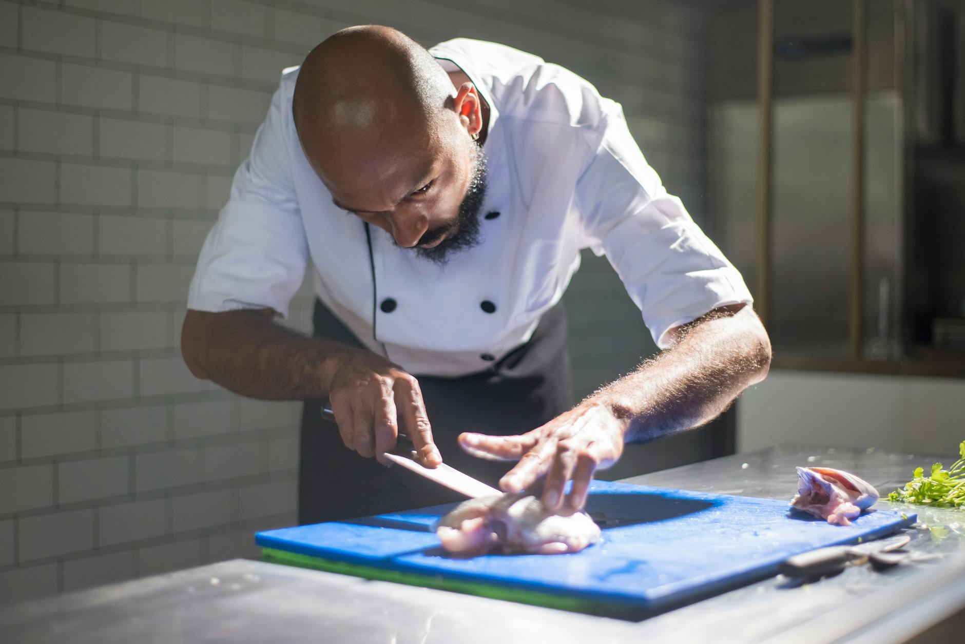 Sharp chef knife being used on a wooden cutting board in a professional kitchen