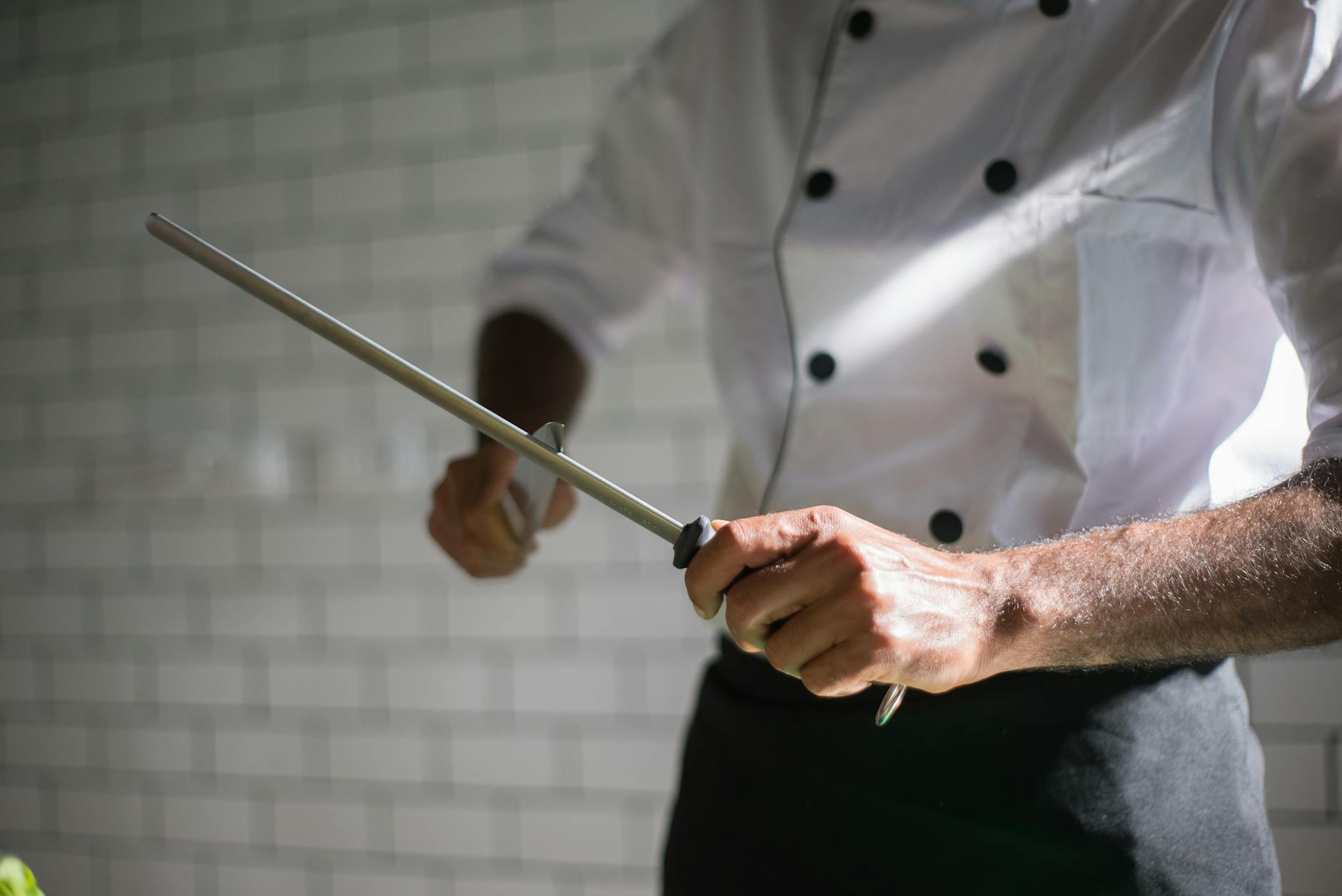 Professional chef using a honing rod to realign a kitchen knife edge