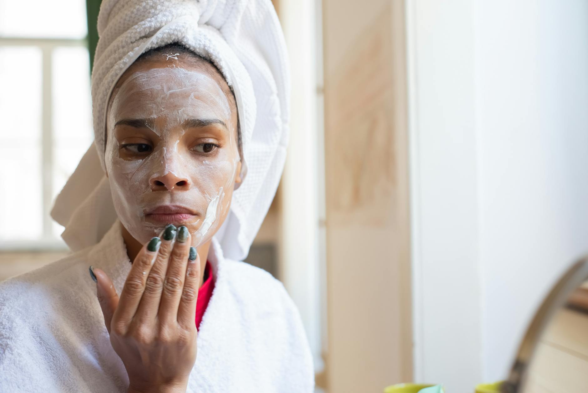 Woman applying skincare products in bathroom as part of her layered morning routine