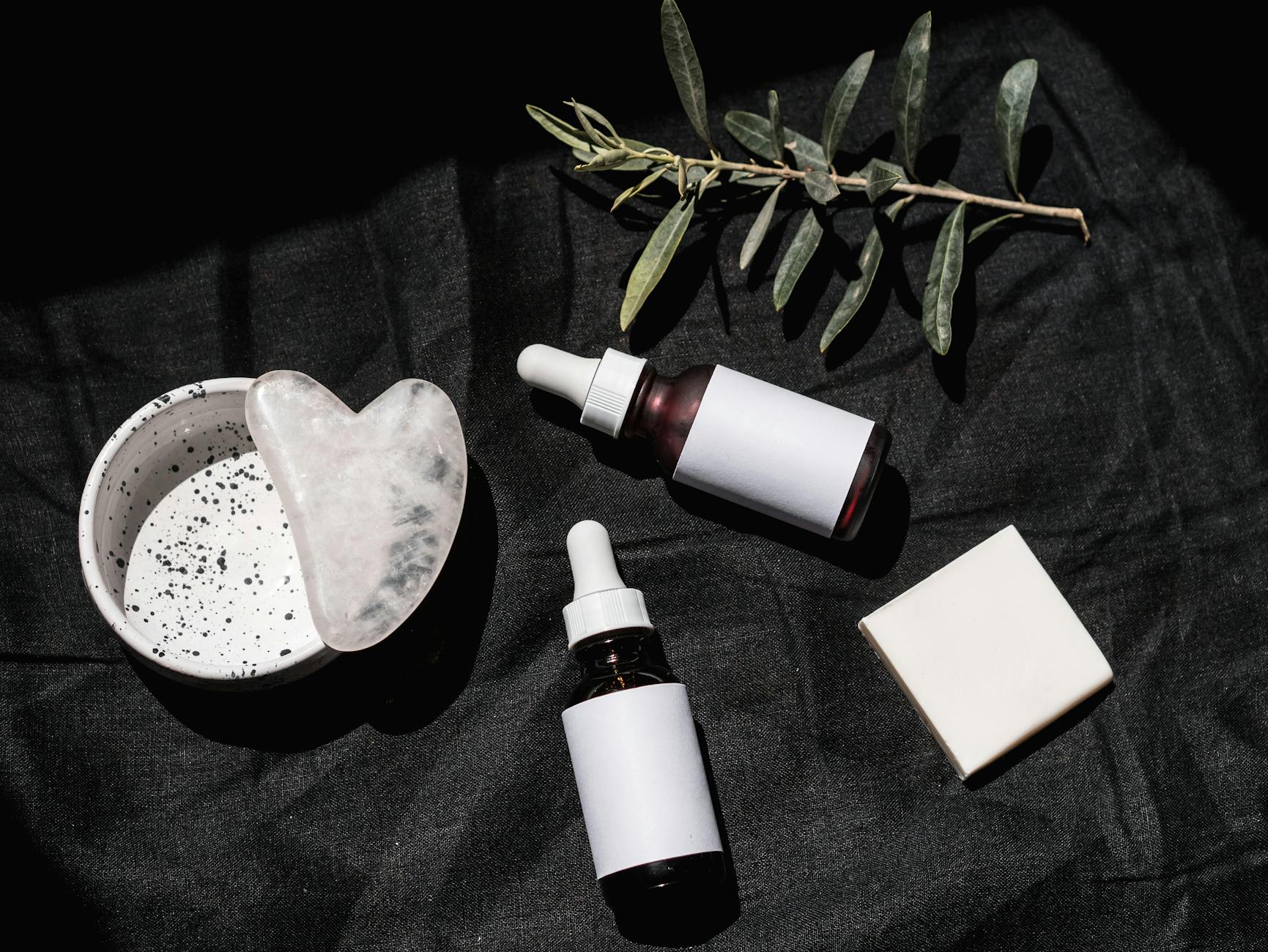 Skincare serums and gua sha tool arranged on black textile, representing a complete skincare routine