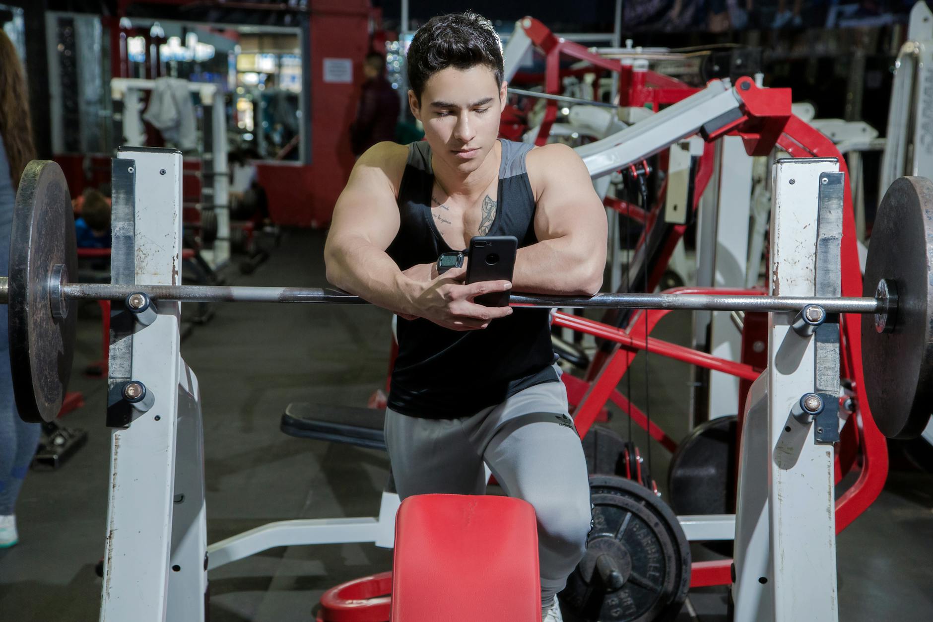 Man resting at the gym while checking his phone near weightlifting equipment