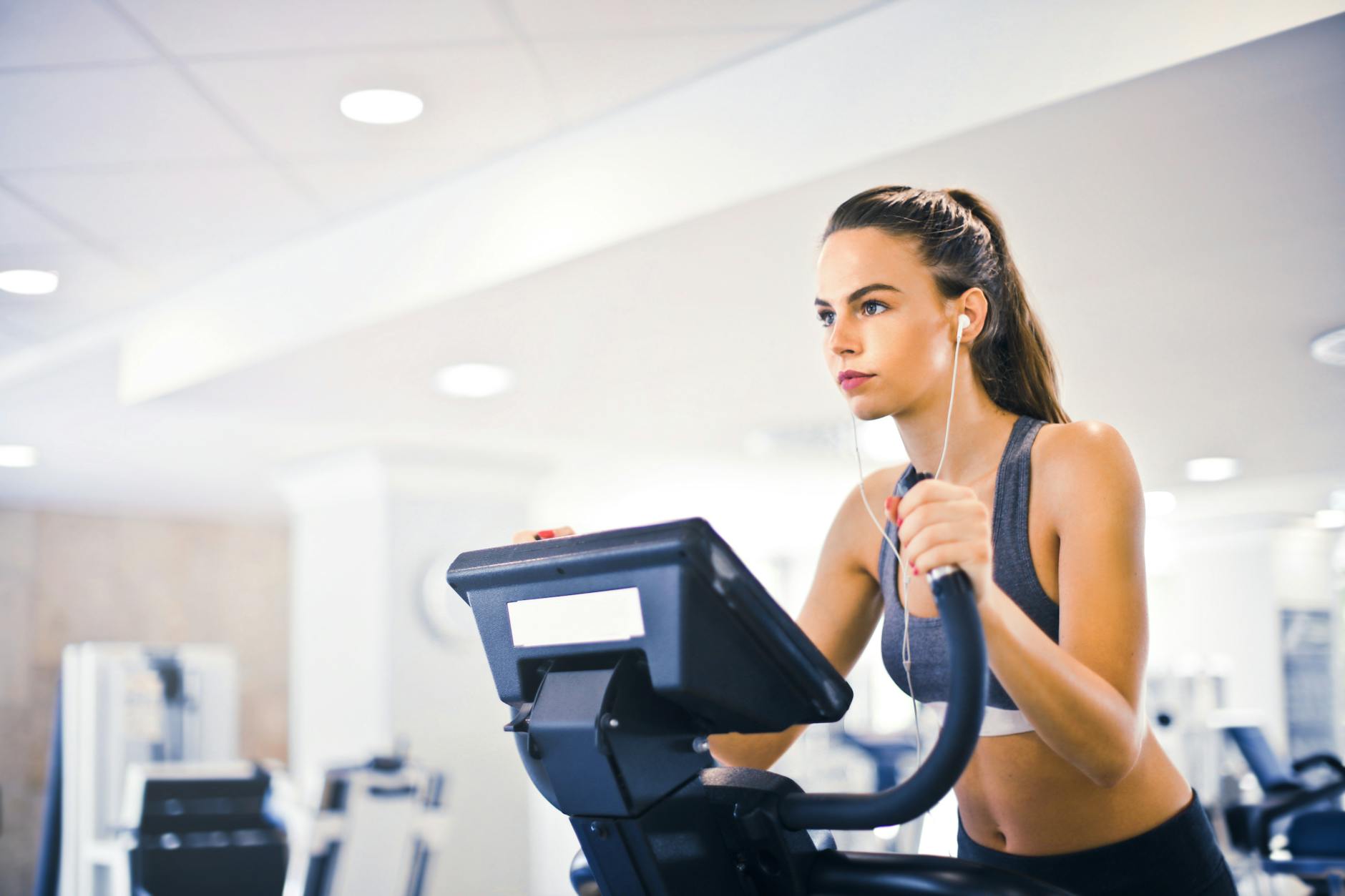 Woman running on treadmill wearing earphones and streaming music on her phone at the gym