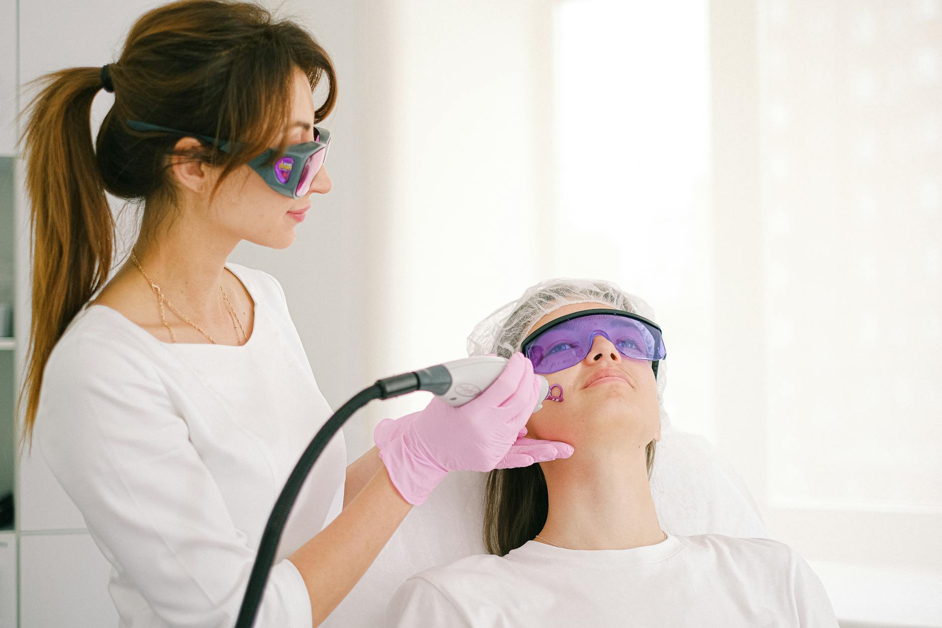 Cosmetologist performing laser facial hair removal treatment on a woman in a professional clinic