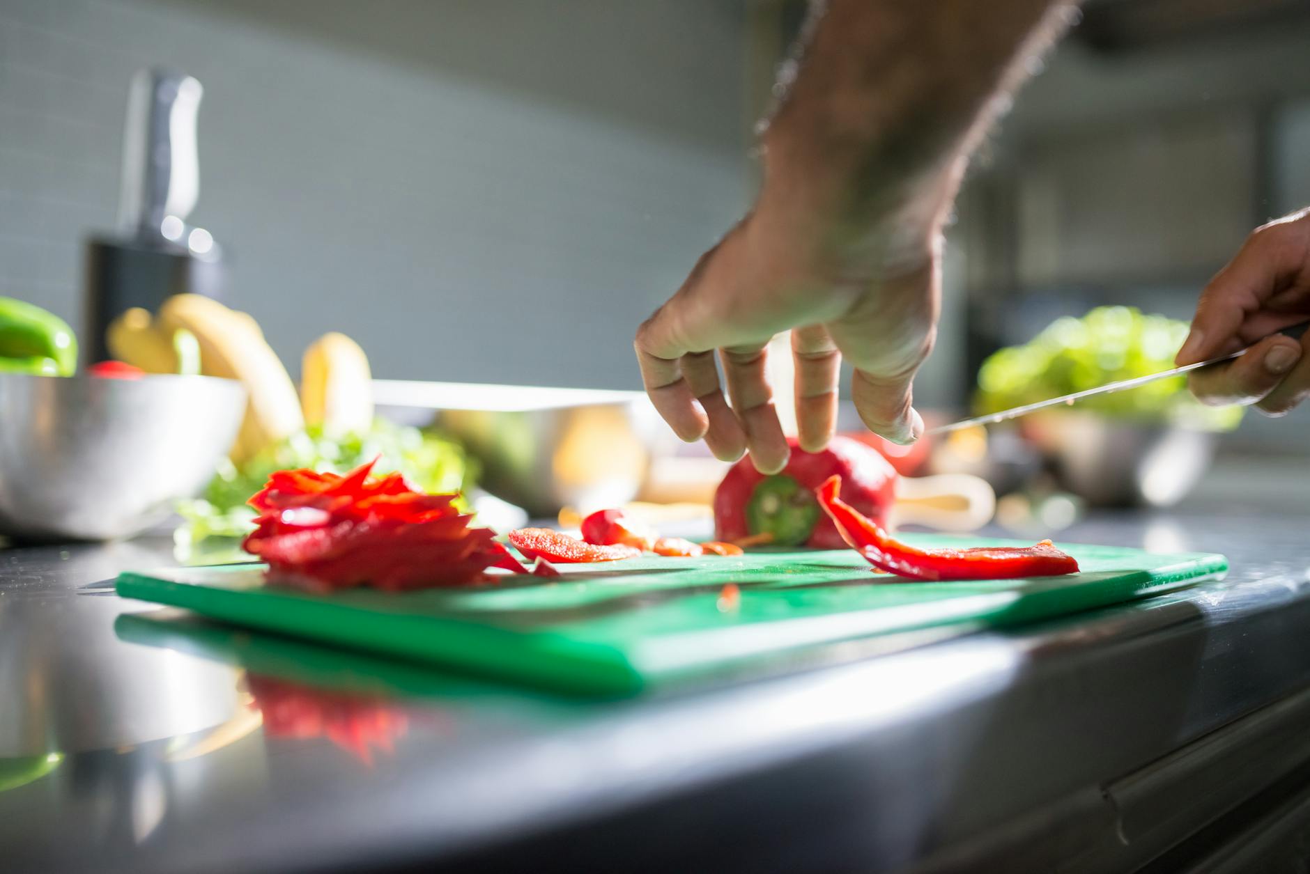 Hands slicing red bell pepper on a plastic chopping board — a common kitchen task that can release microplastic particles