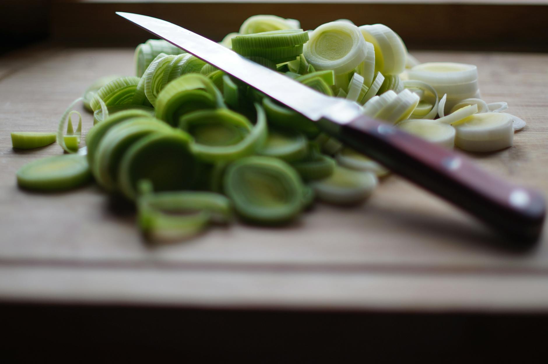 Freshly sliced leeks on a wooden cutting board with a knife — a plastic-free cutting surface alternative