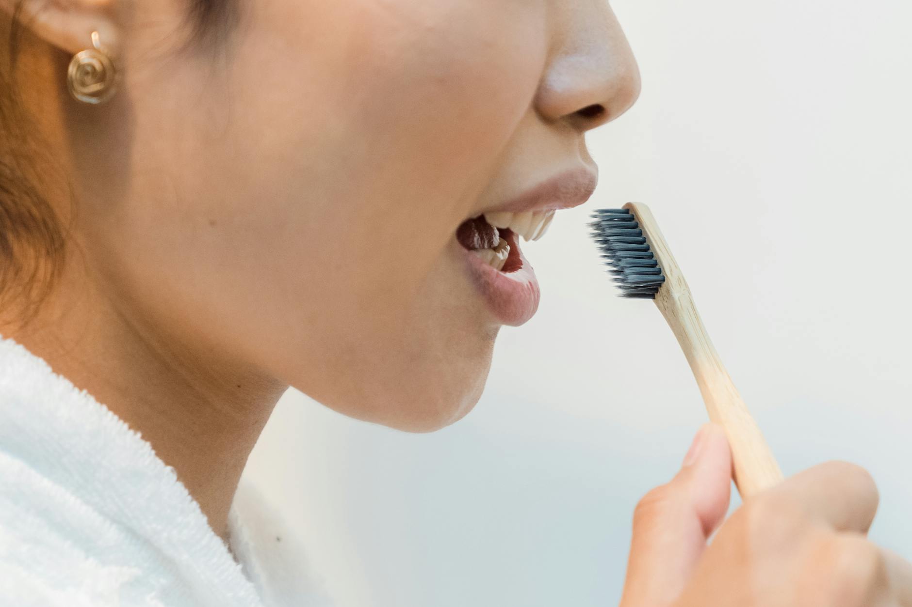 Removing Oral Bacteria Through Consistent Brushing 2026 Woman brushing teeth with bamboo toothbrush to remove oral bacteria and plaque biofilm