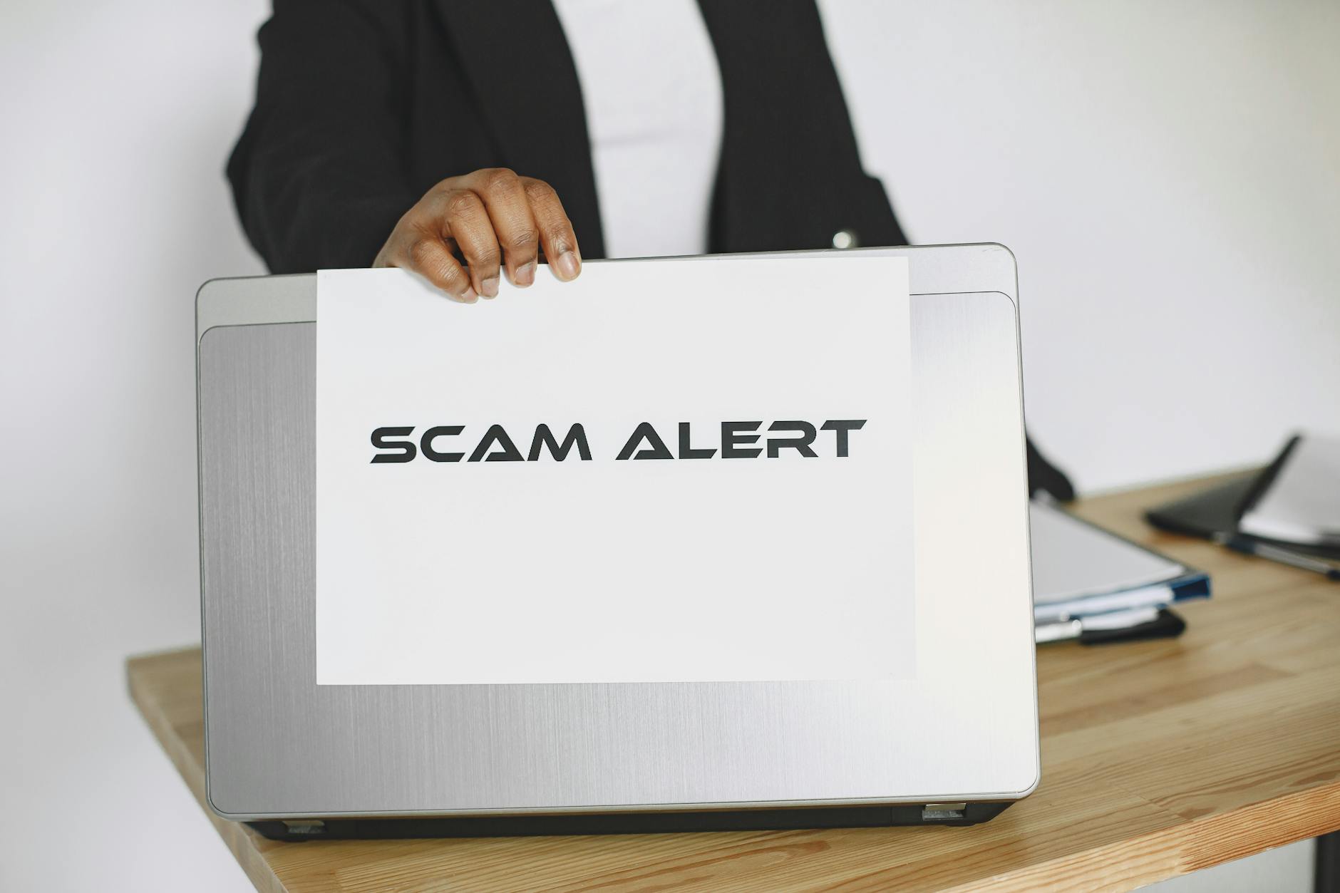 Person holding a scam alert sign over a laptop, illustrating online fraud awareness