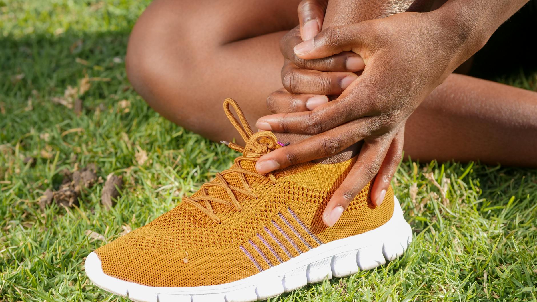Athlete Experiencing Foot and Ankle Pain Requiring Rest and Treatment Athlete on grass holding their ankle after foot pain, illustrating the need for activity modification during plantar fasciitis recovery