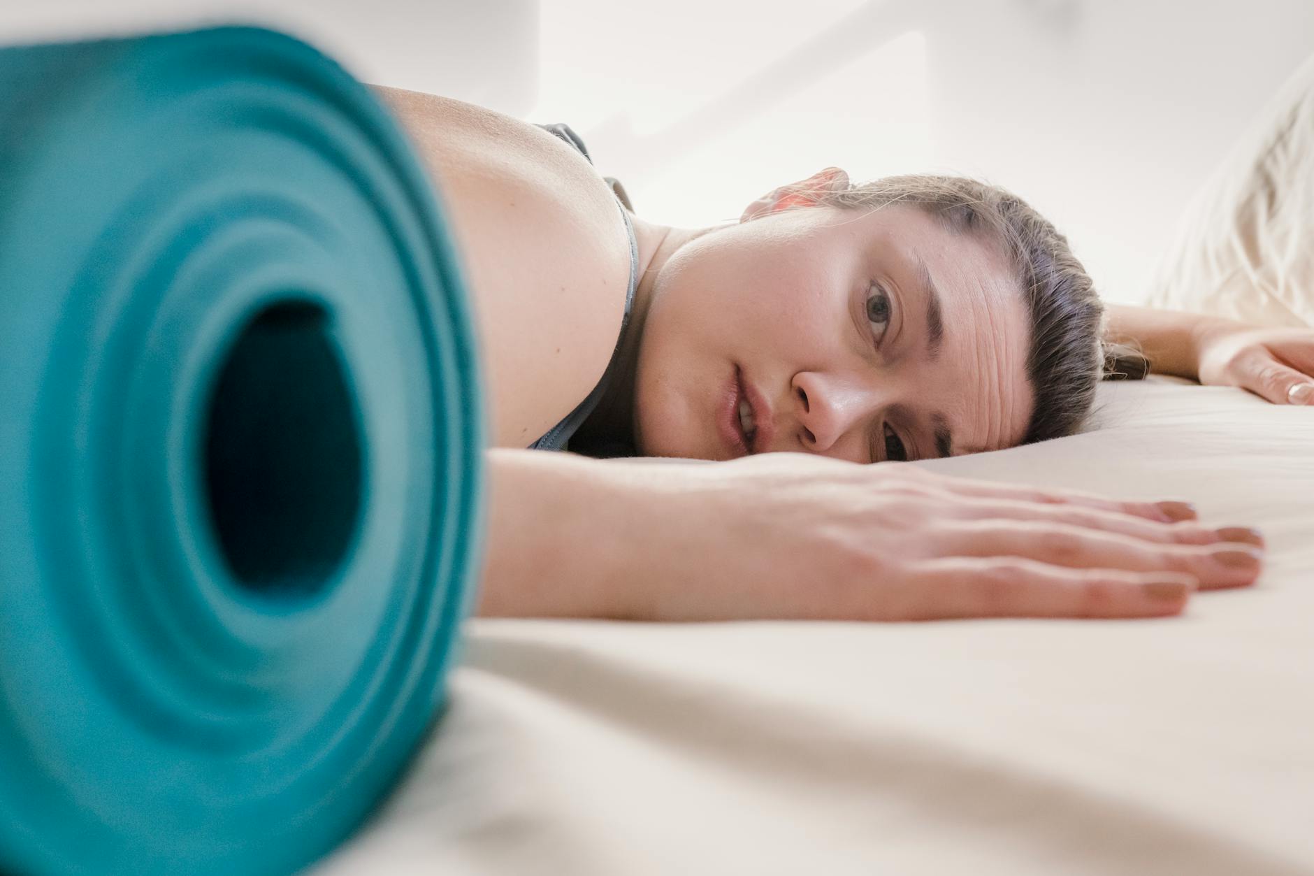 Woman resting after exercise near a yoga mat, illustrating post-workout recovery