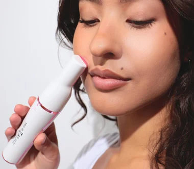 Pluxy promotional photo of a woman holding the facial epilator beside her cheek